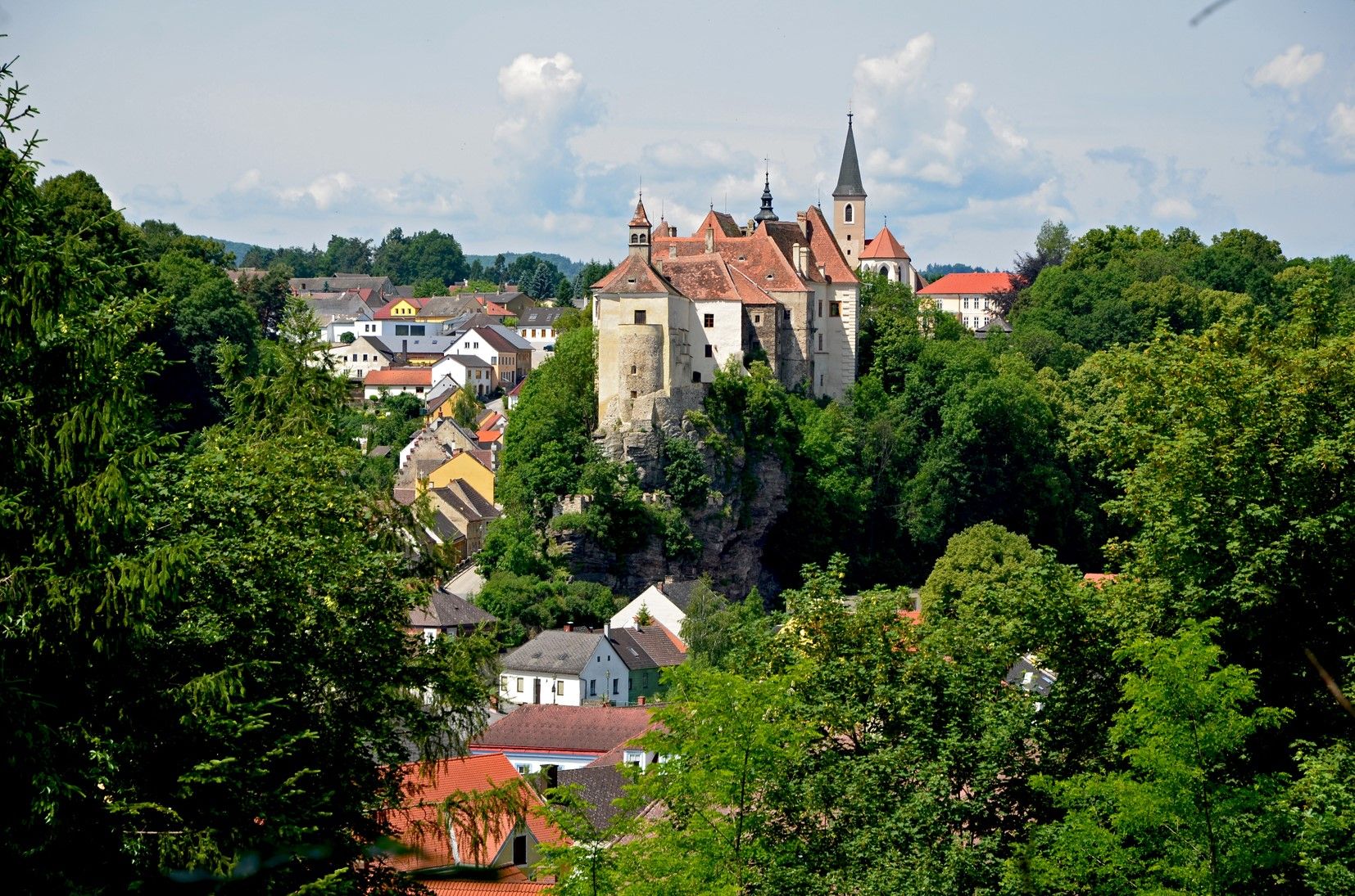 Blick auf die Stadt Raabs mit einer Burg auf einem Hügel, umgeben von Bäumen und Häusern.
