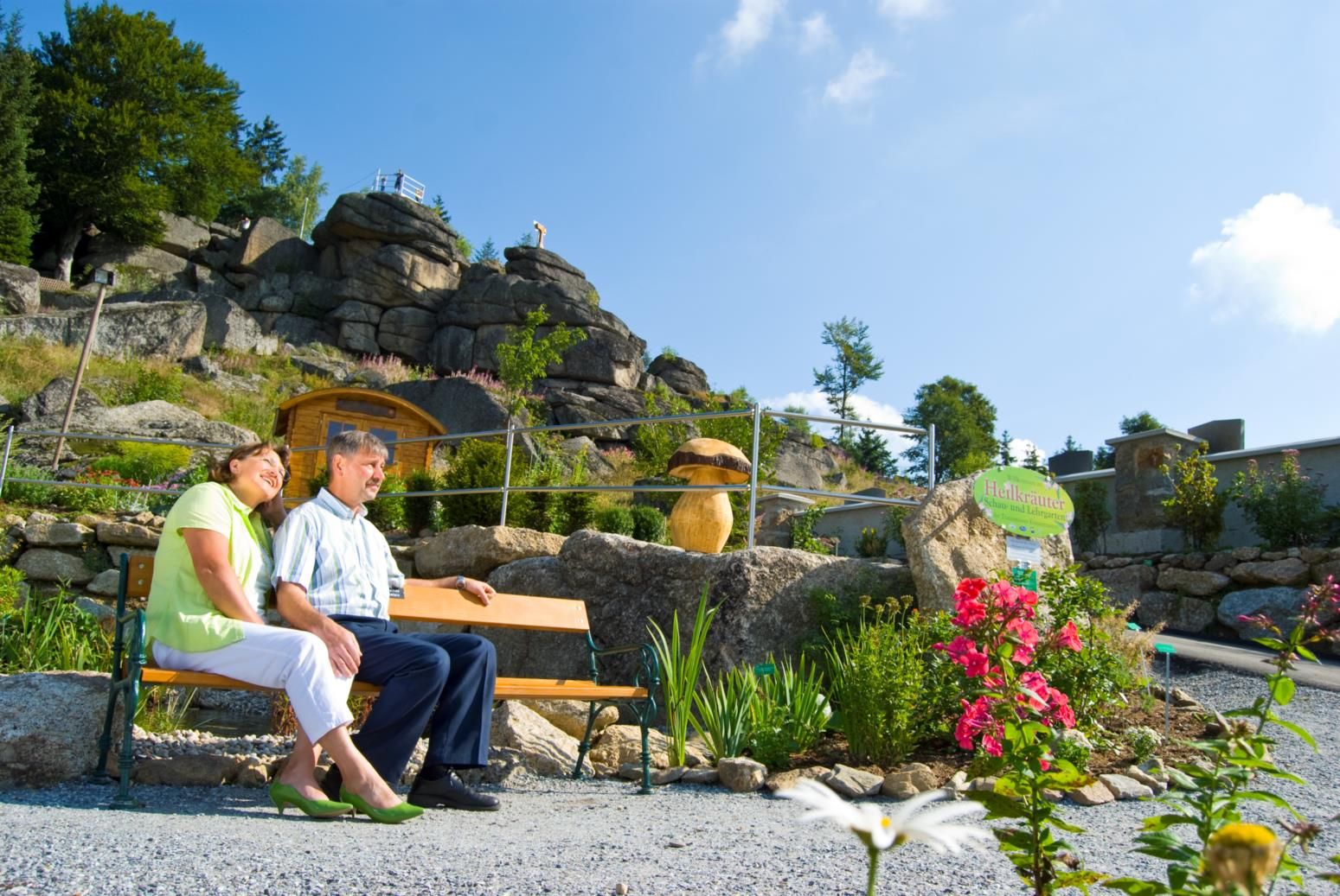 Ein Paar sitzt auf einer Bank in einem Kräutergarten mit Felsen im Hintergrund.