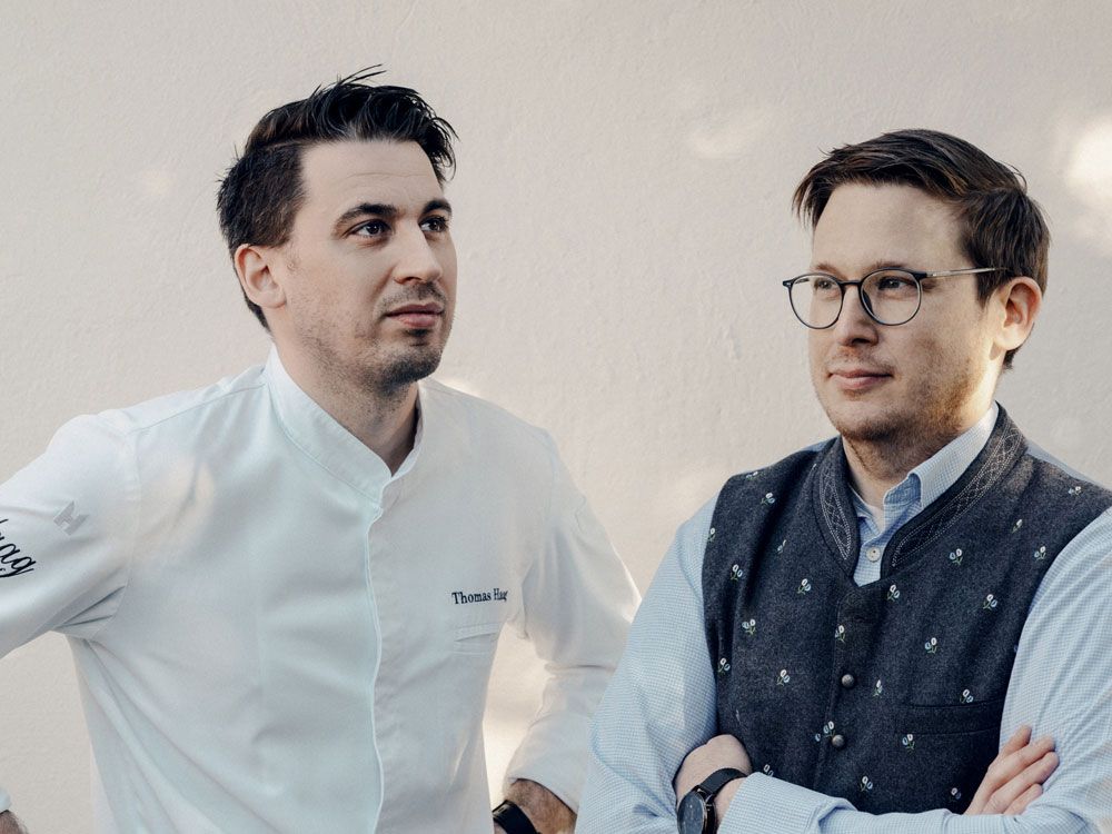 Zwei Männer stehen nebeneinander, einer trägt eine Kochjacke, der andere eine Trachtenweste.