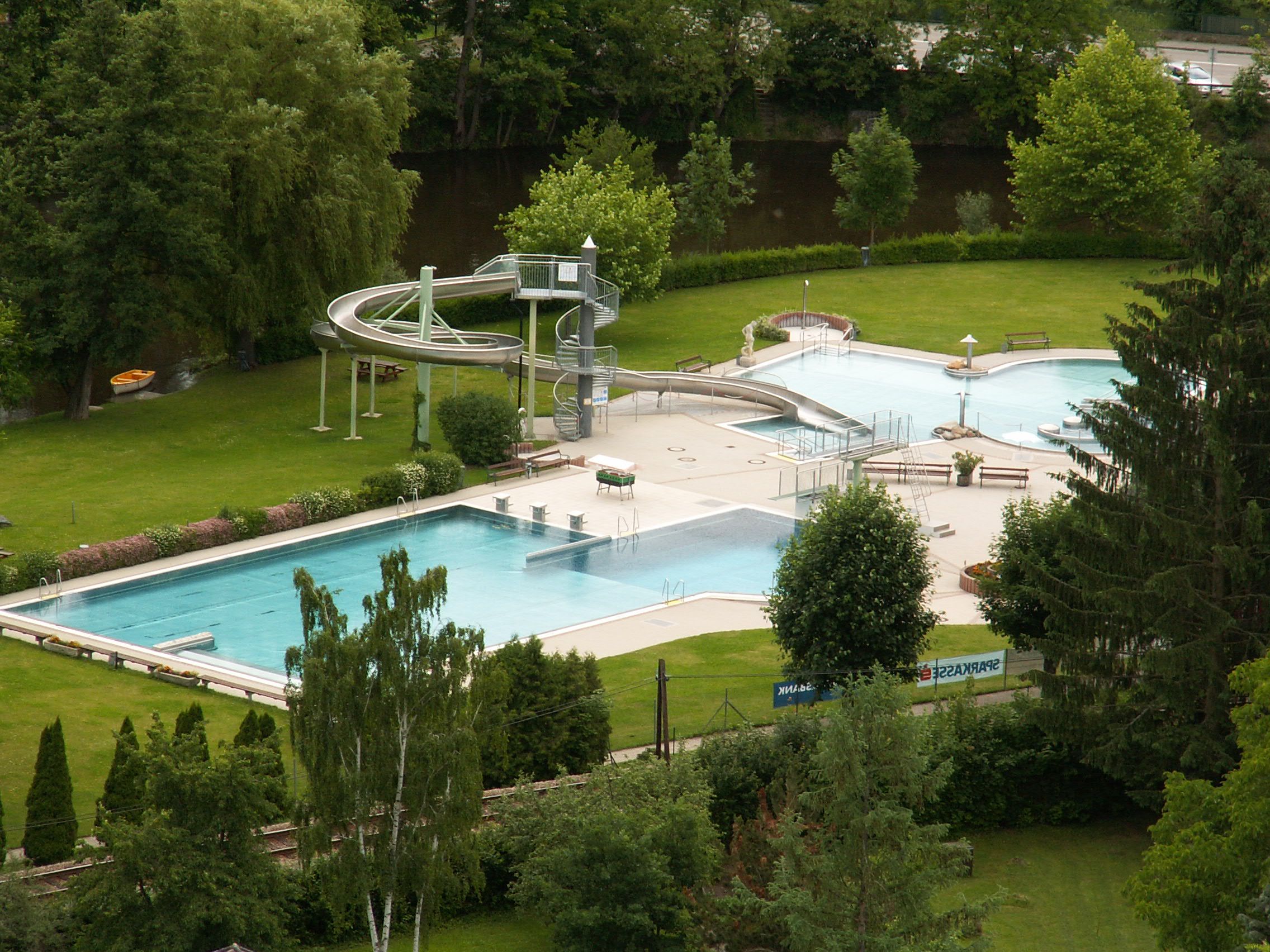 Luftaufnahme eines Freibads mit Rutsche und Becken, umgeben von Bäumen.