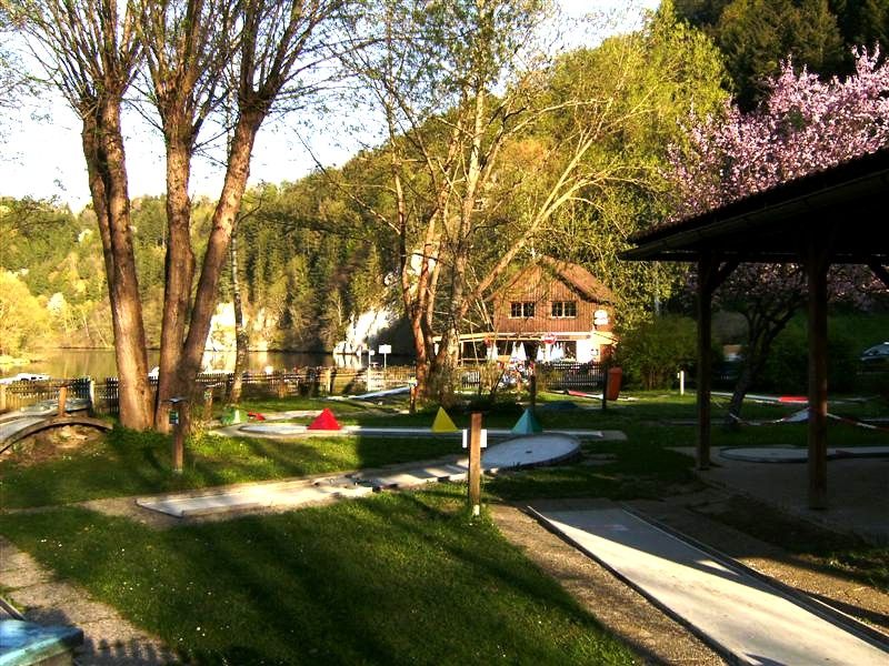 Miniaturgolfplatz mit Bäumen und einem Gebäude im Hintergrund.