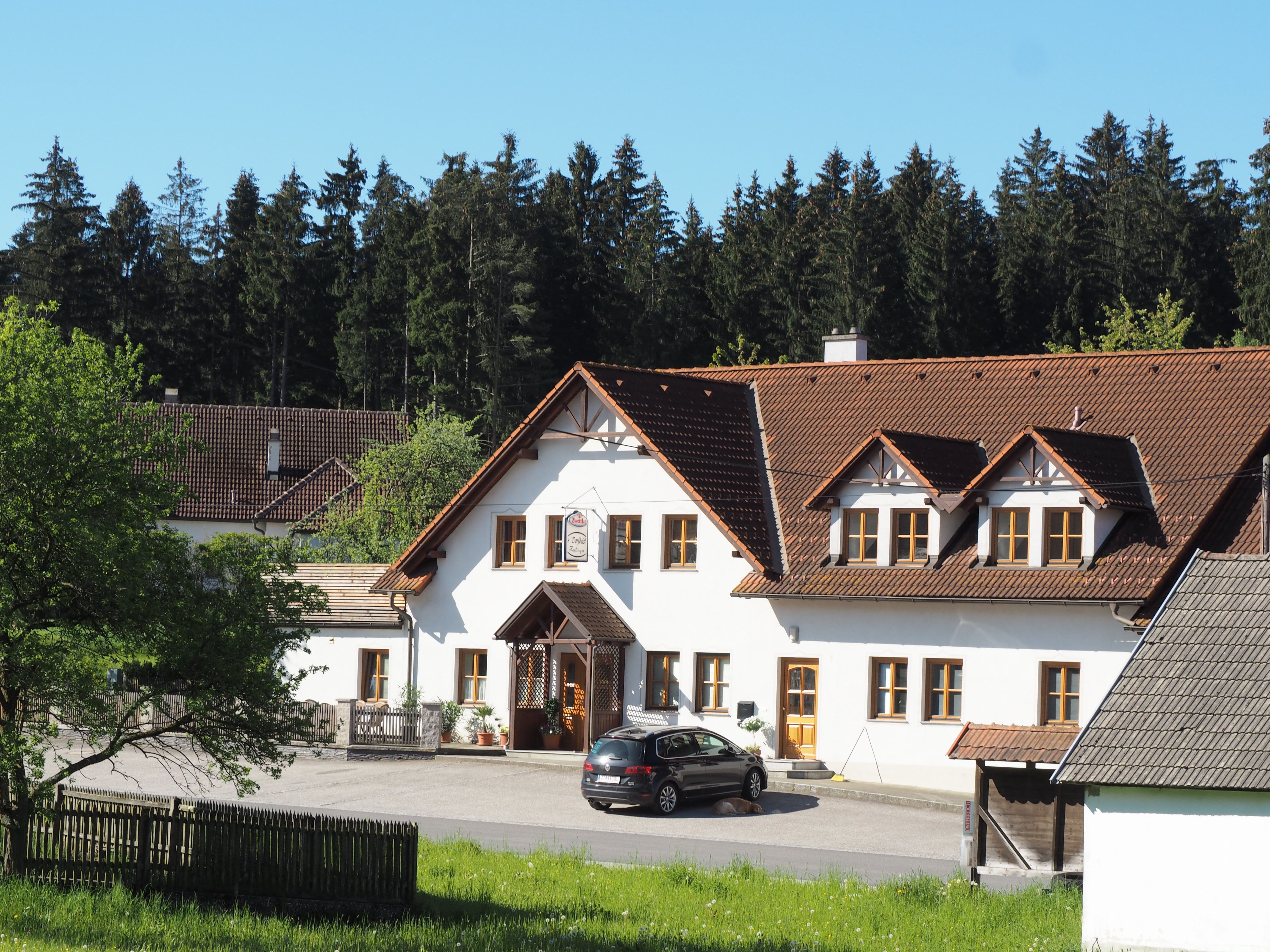 Ein traditionelles Gasthaus mit weißer Fassade und braunem Dach, umgeben von Bäumen und Wiese.