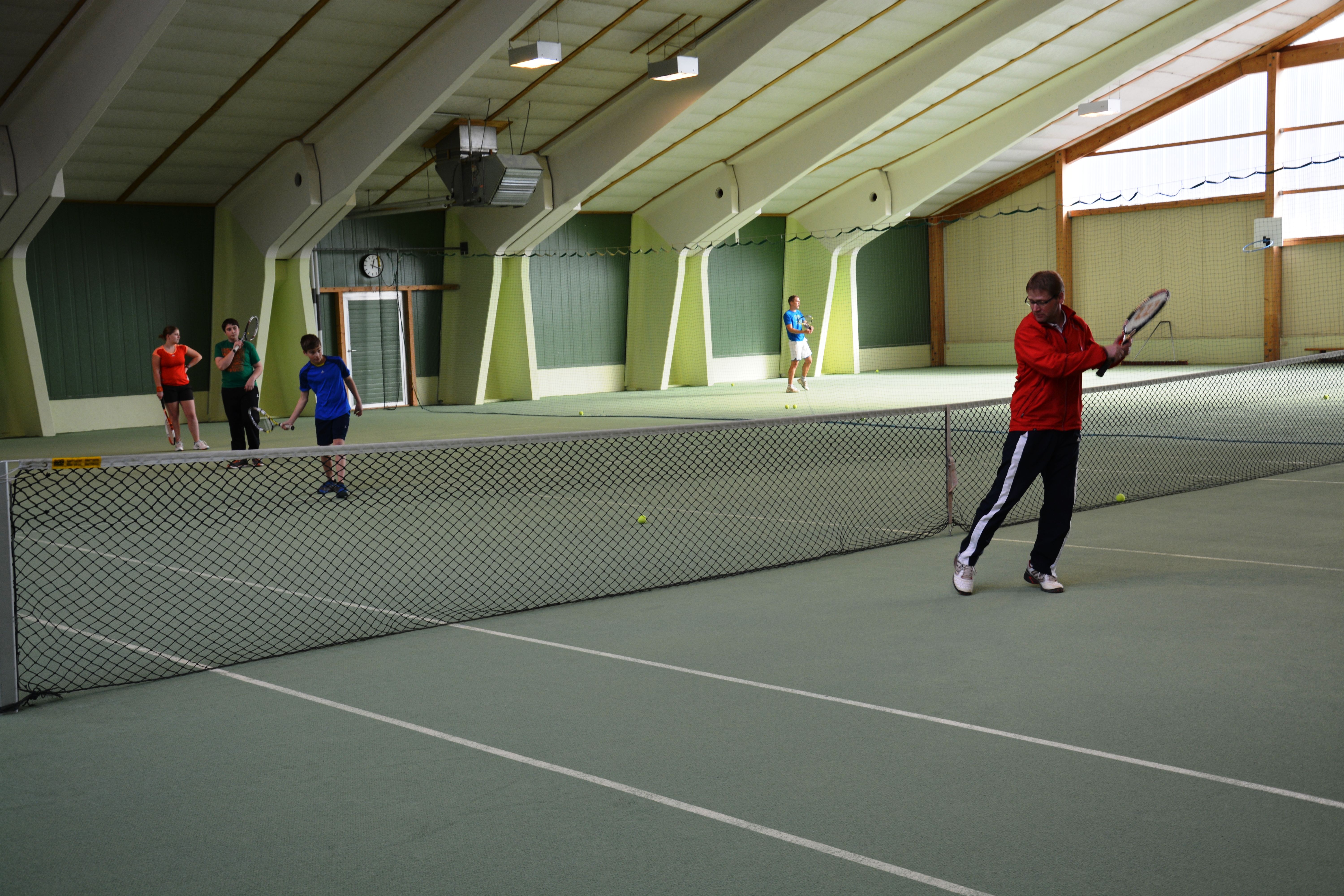 Personen spielen Tennis in einer Tennishalle.