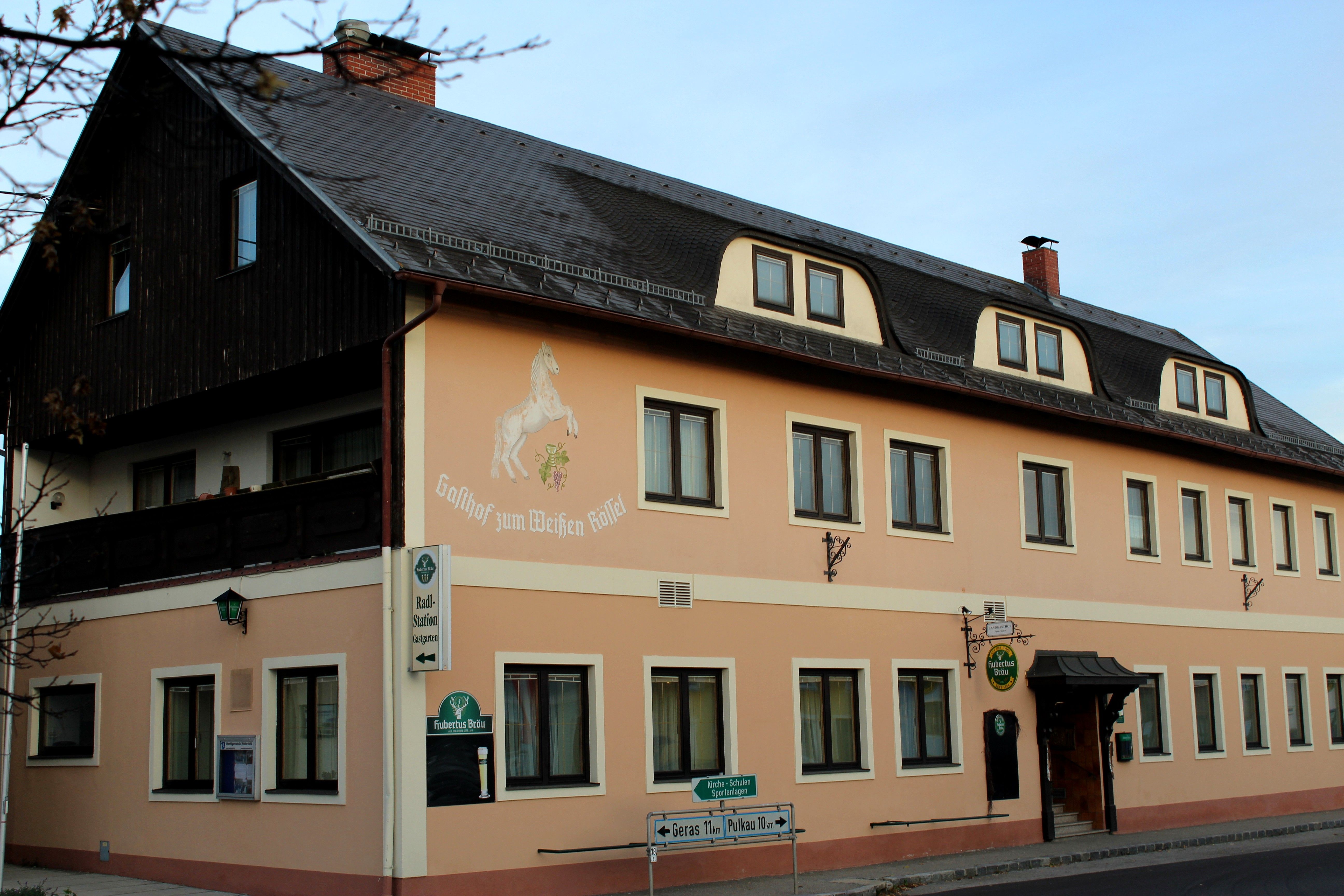 Außenansicht des Gasthofs 'Zum weißen Rössel' mit beige Fassade und Pferdemalerei.