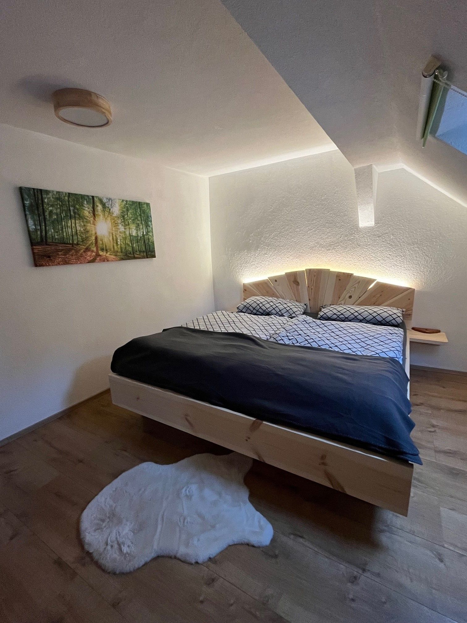 Ein gemütliches Schlafzimmer mit einem Holzbett, einem Bild von einem Wald an der Wand und einem weißen Teppich auf dem Holzboden.