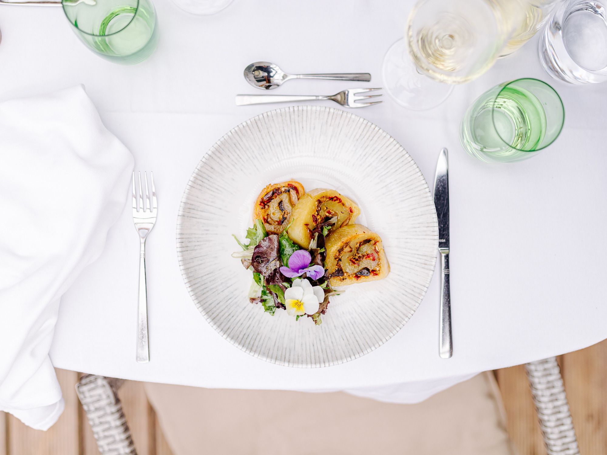 Ein Teller mit gefüllter Erdäpfelroulade und Salat auf einem gedeckten Tisch.