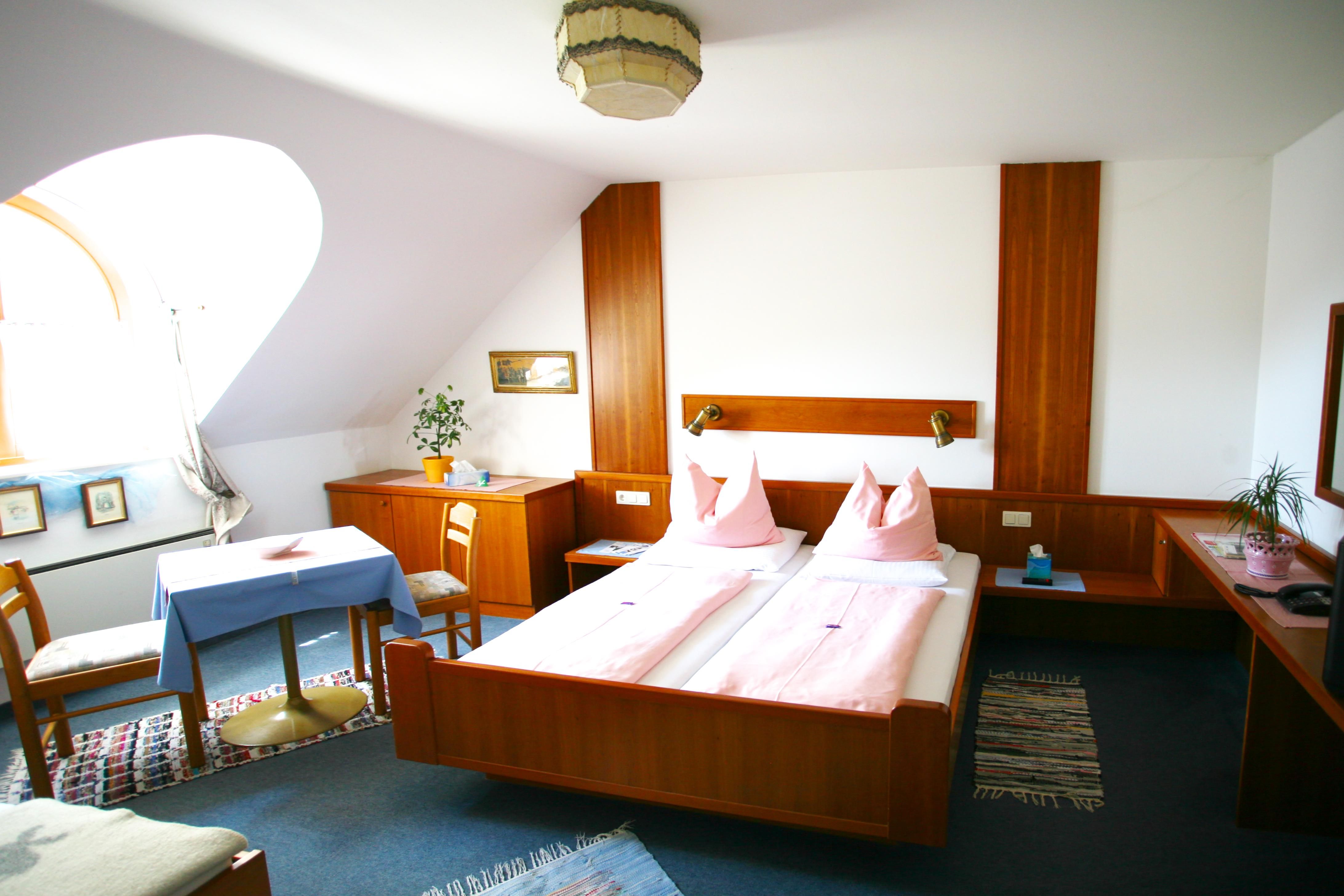 Gemütliches Hotelzimmer mit Doppelbett, Holzmöbeln und Tisch mit Stühlen.