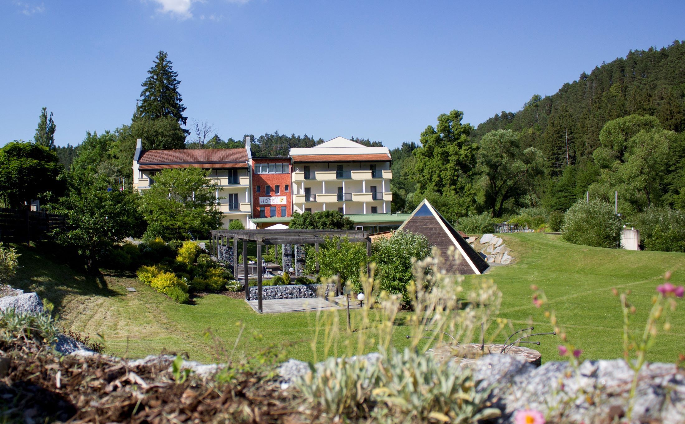 Hotelgebäude mit Garten und Pavillon, umgeben von Bäumen.