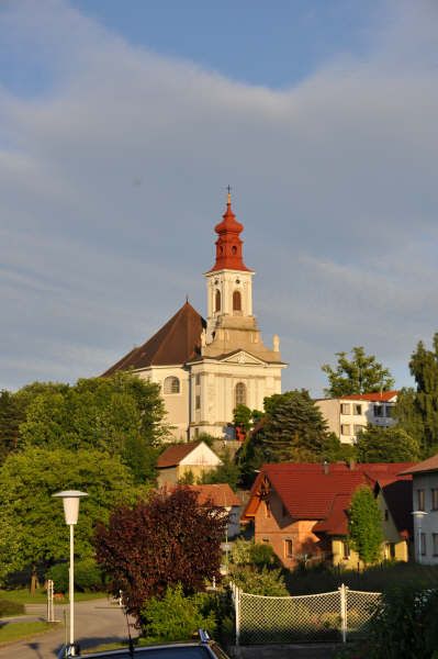Wallfahrtskirche auf einem Hügel mit roten Dächern und Bäumen im Vordergrund.
