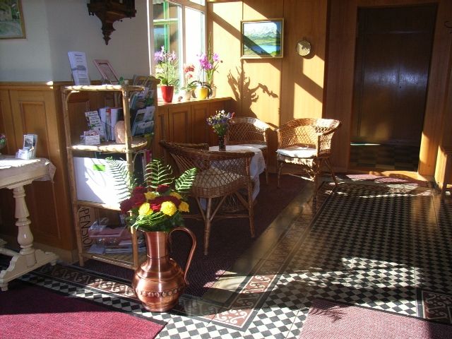 Eingangshalle einer Pension mit Korbmöbeln, Blumen und dekorativem Bodenmuster.