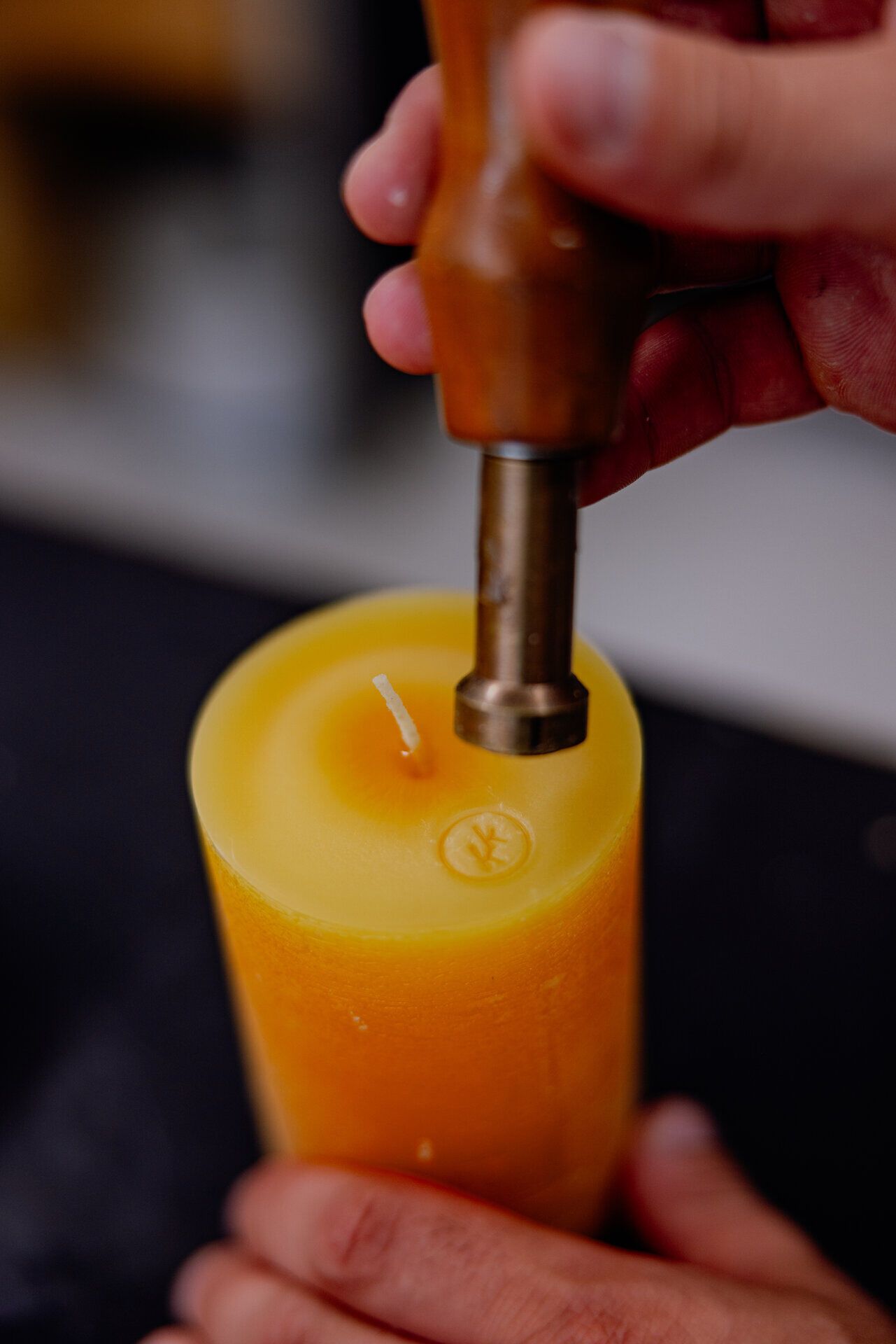 In einer warmen, einladenden Atmosphäre wird eine handgefertigte Kerze mit einem speziellen Werkzeug verziert. Die sanften Gelbtöne des Wachses strahlen Ruhe und Gemütlichkeit aus, während die geschickten Hände des Handwerkers die Tradition des Kerzenmachens lebendig halten.