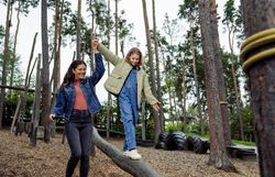 Ein fröhliches Abenteuer erwartet die Familie im Waldviertel, während sie über einen Baumstamm balanciert. Die Kinder lachen und genießen die frische Luft, umgeben von hohen Bäumen und der Schönheit der Natur. Hier wird der Sommer in den Bergen lebendig und unvergesslich.