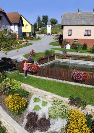 Ein gepflegter Garten mit Blumenbeeten und einem kleinen Teich in einem Dorf.