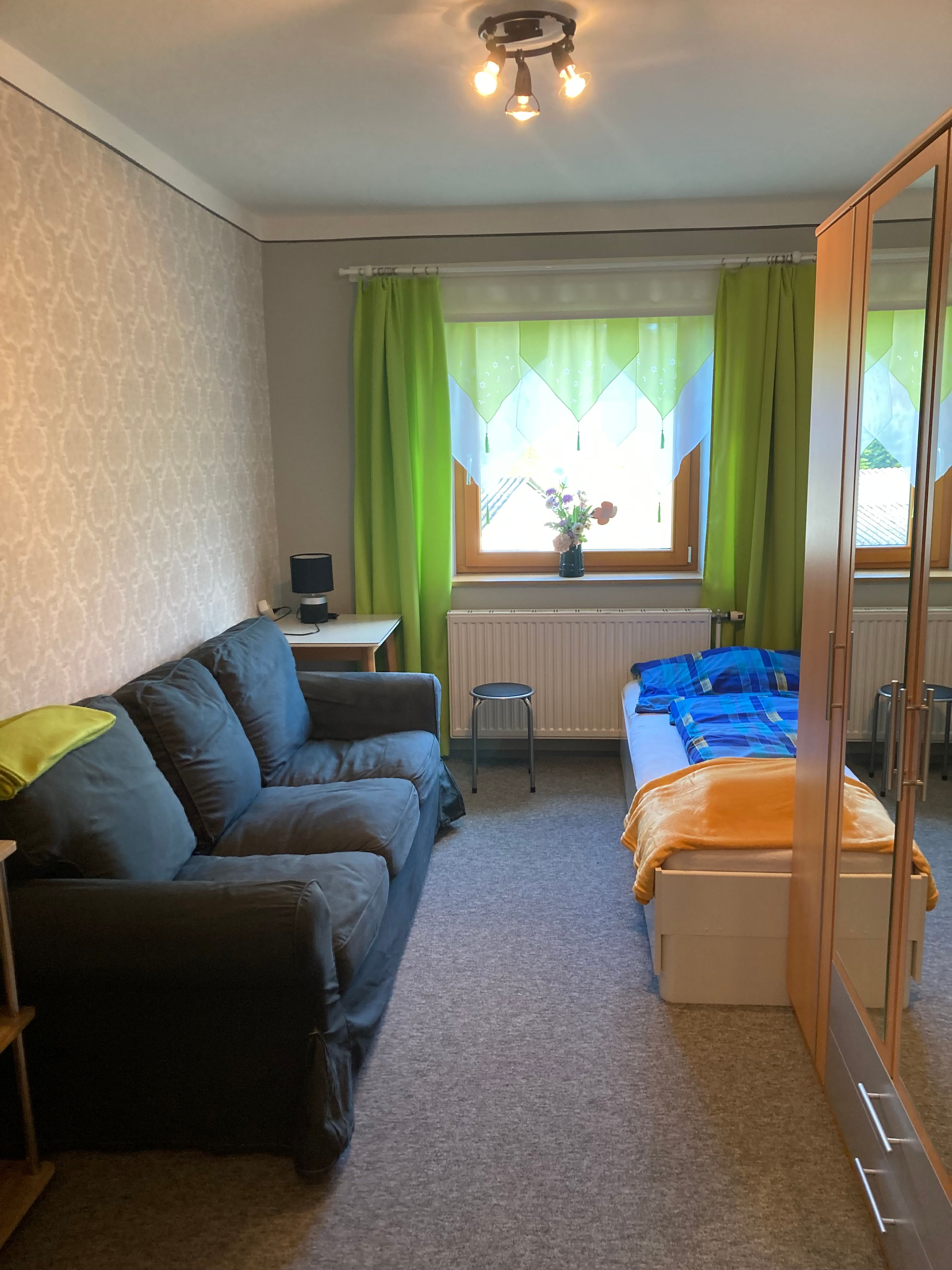 Ein gemütliches Schlafzimmer mit Sofa, Bett, Schrank und grünem Vorhang.