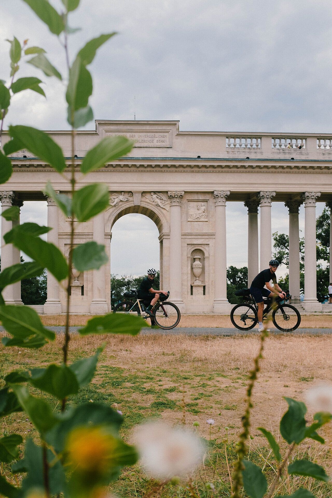Radfahrer gleiten entspannt entlang der malerischen Landschaft, umgeben von üppigem Grün und historischen Säulen. Die sanfte Brise und die beeindruckenden Ausblicke laden dazu ein, die Schönheit der Natur in vollen Zügen zu genießen.
