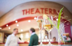 In der einladenden Atmosphäre der Theaterbar genießen Gäste prickelnde Getränke, während im Hintergrund angeregte Gespräche über die neuesten Kulturhighlights stattfinden. Die stilvolle Einrichtung und die sanfte Beleuchtung schaffen einen perfekten Ort, um den Abend zu verbringen und sich auf das bevorstehende Theaterstück zu freuen.