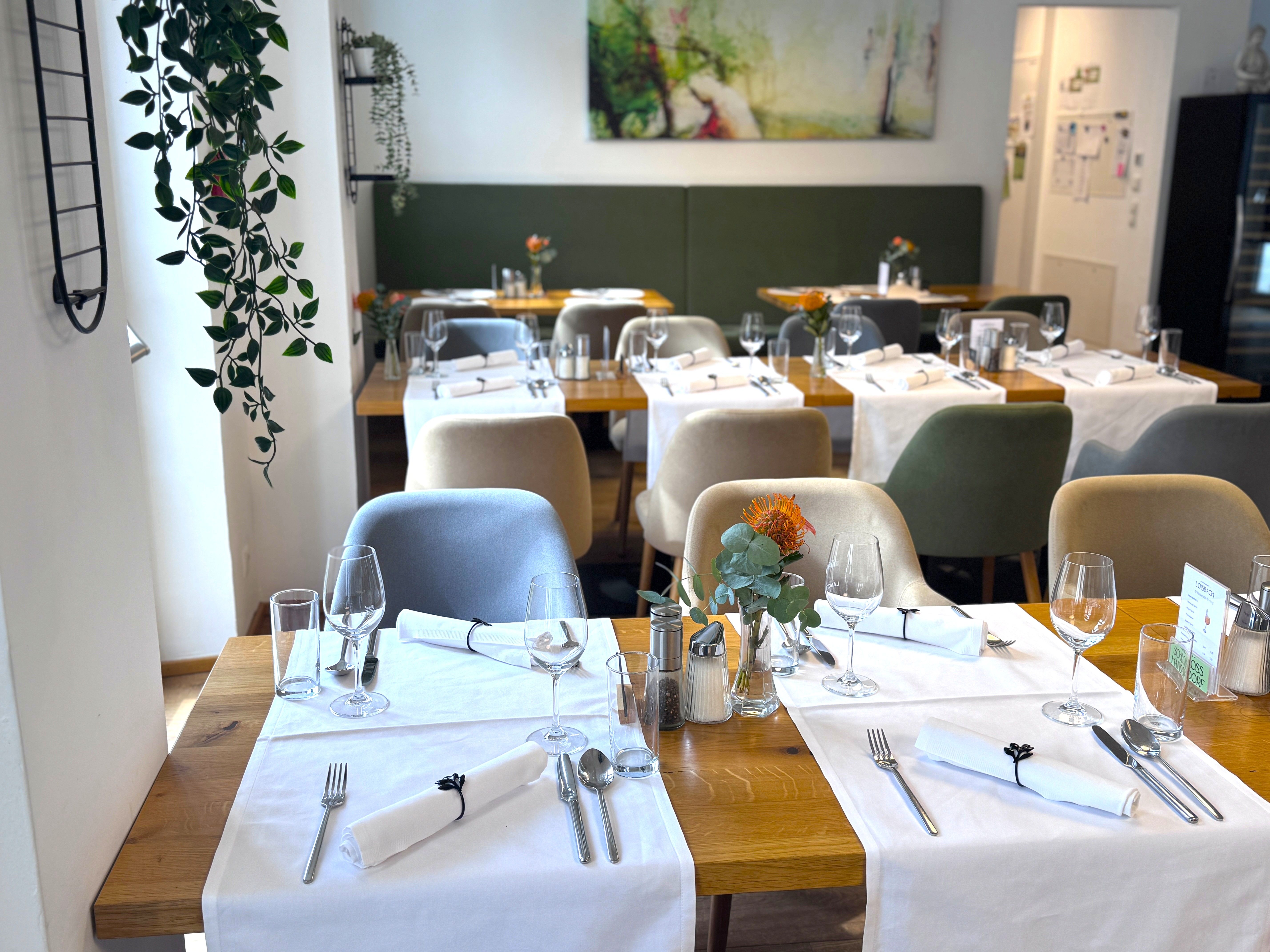 Eingedeckter Restaurantbereich mit gedeckten Tischen, Gläsern, Besteck und Stühlen in einem hellen Raum.