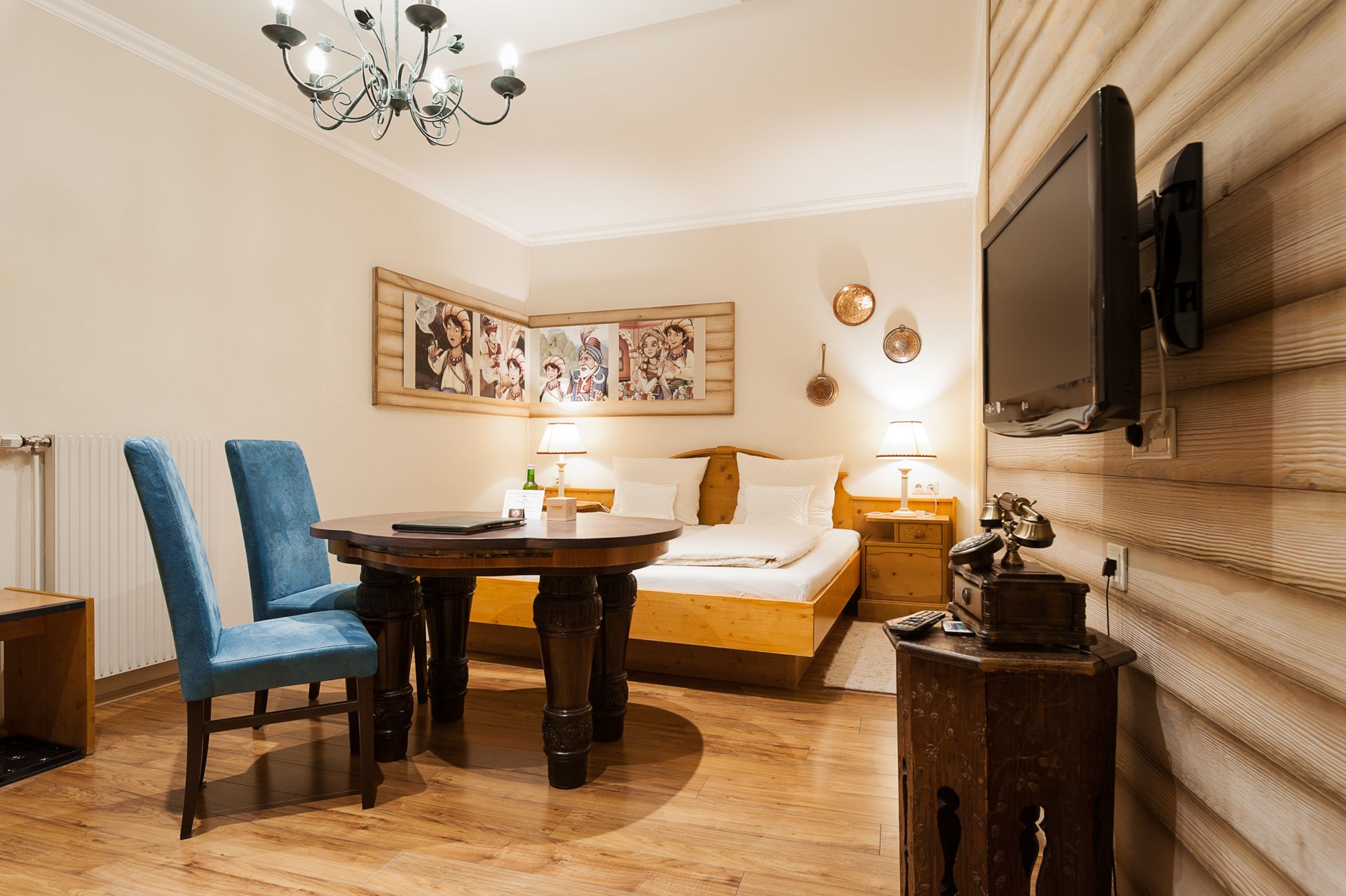 Ein gemütliches Hotelzimmer mit Holzmöbeln, einem Doppelbett, blauen Stühlen, einem runden Tisch und einem Flachbildfernseher an der Wand.