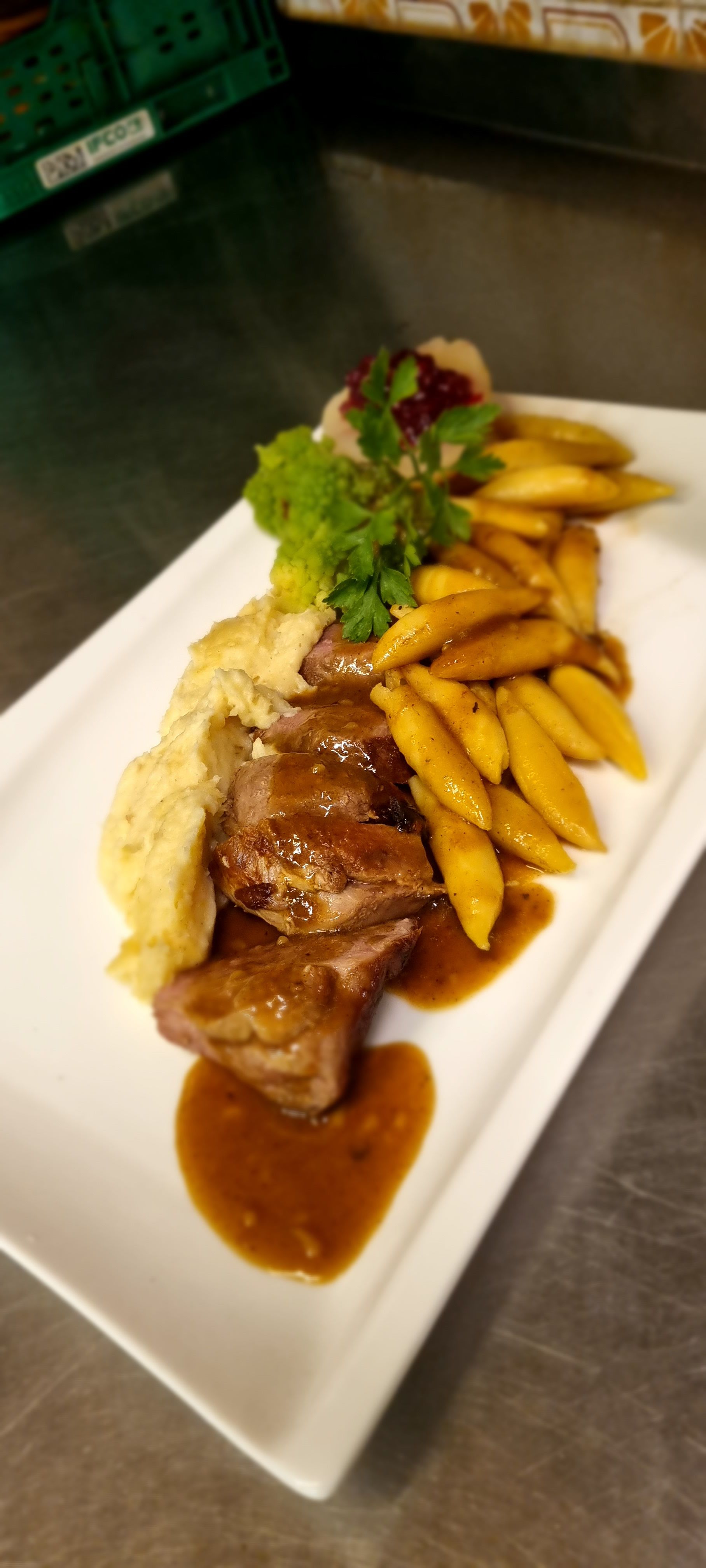 Ein Teller mit Fleisch, Kartoffelpüree, gelben Bohnen und einer braunen Soße, garniert mit Petersilie.