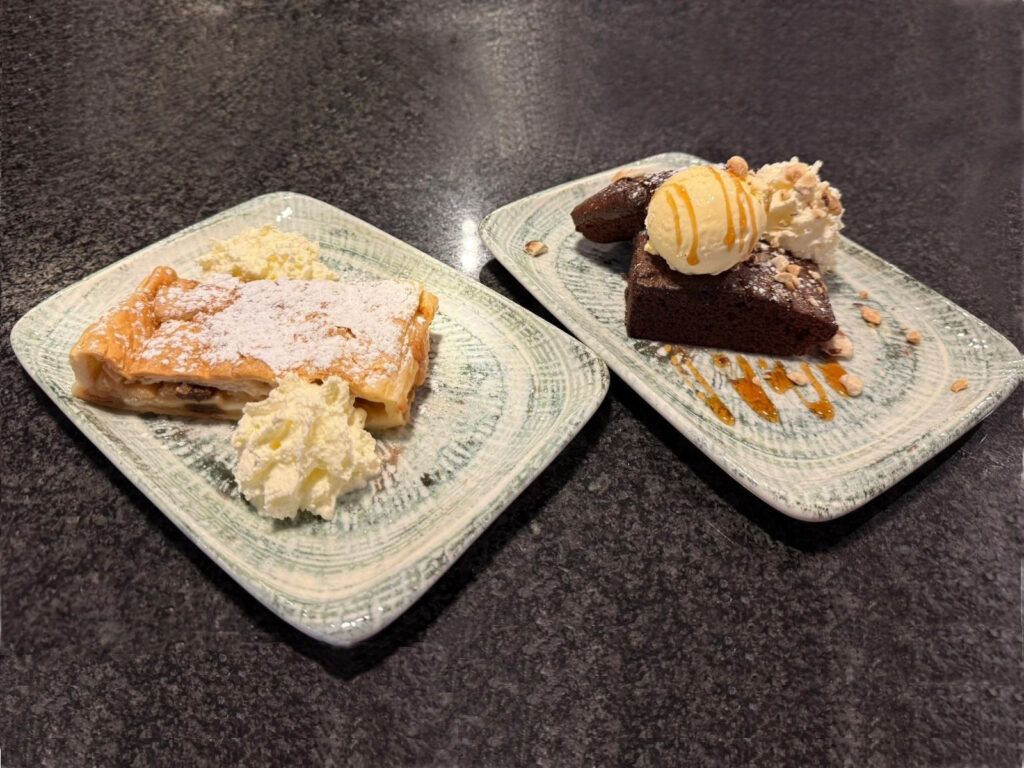 Zwei Dessertteller mit Apfelstrudel und Schokoladenkuchen auf einem dunklen Tisch.