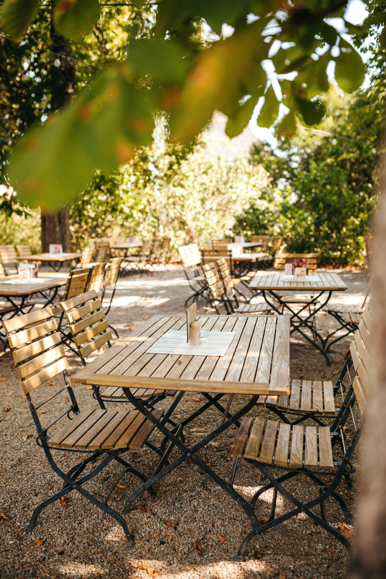 Ein Gastgarten mit Holztischen und -stühlen unter Kastanienbäumen.