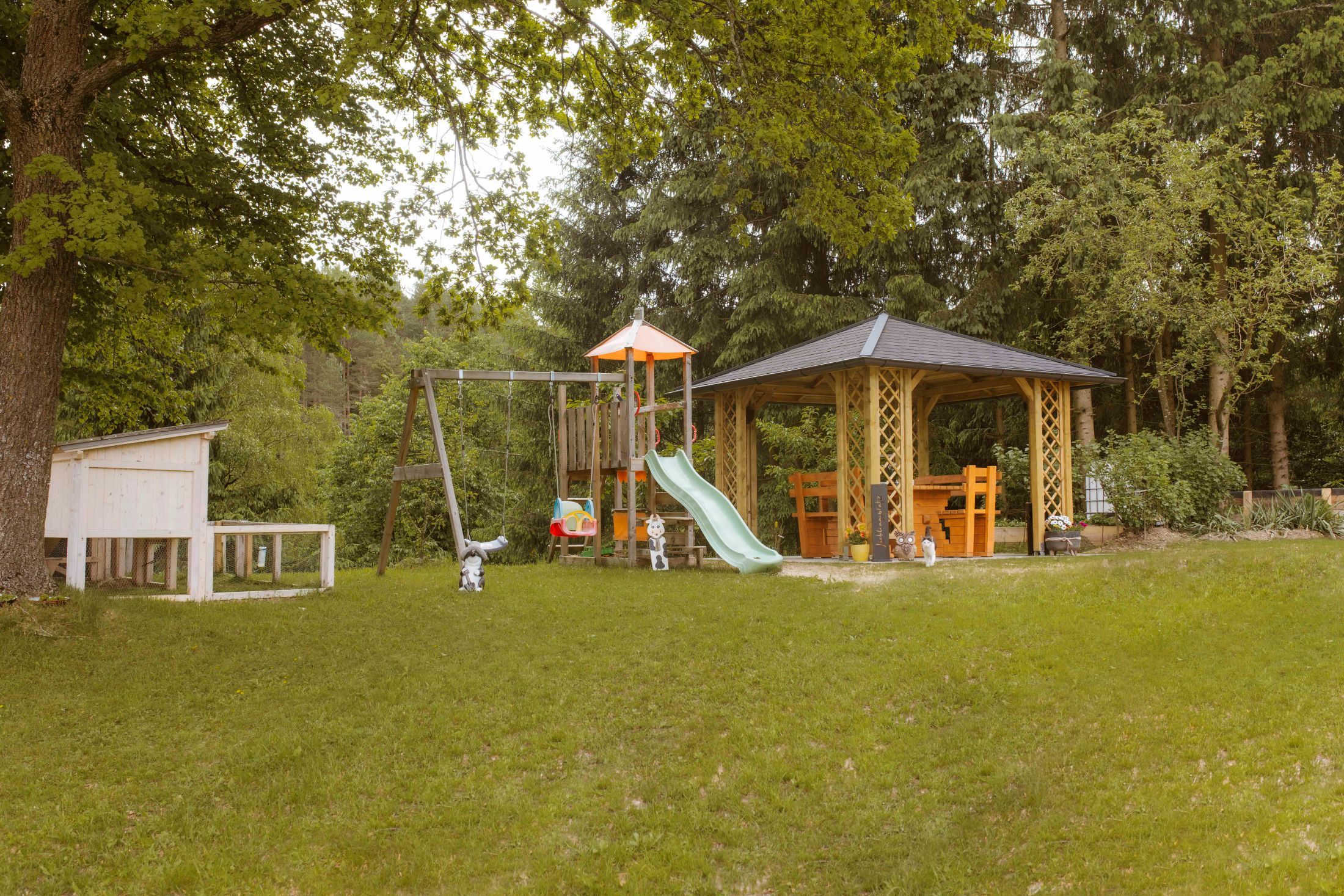 Ein Spielplatz mit Schaukel, Rutsche und Pavillon in einem grünen Garten.