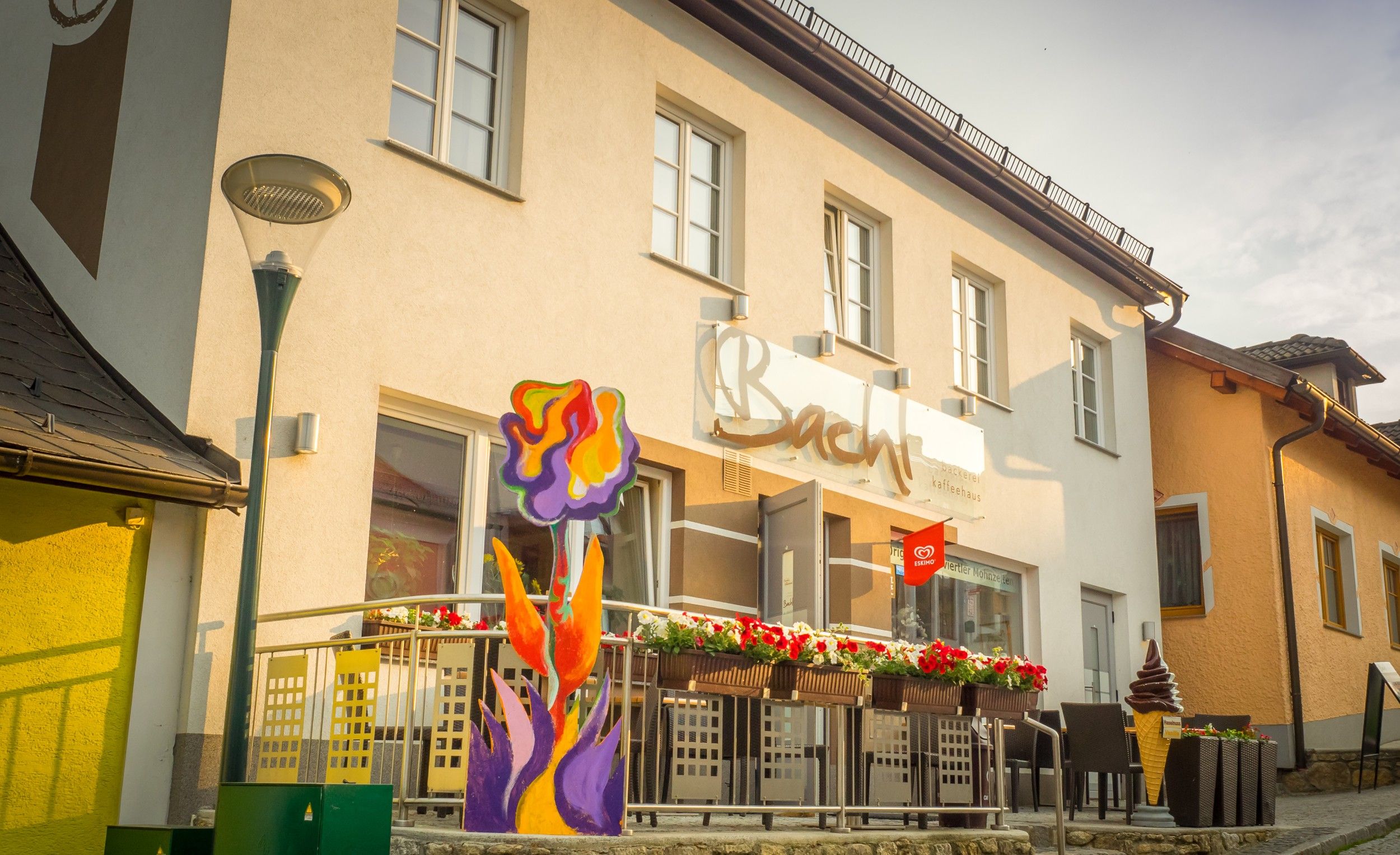 Außenansicht eines Cafés mit Terrasse und bunter Blumendekoration.