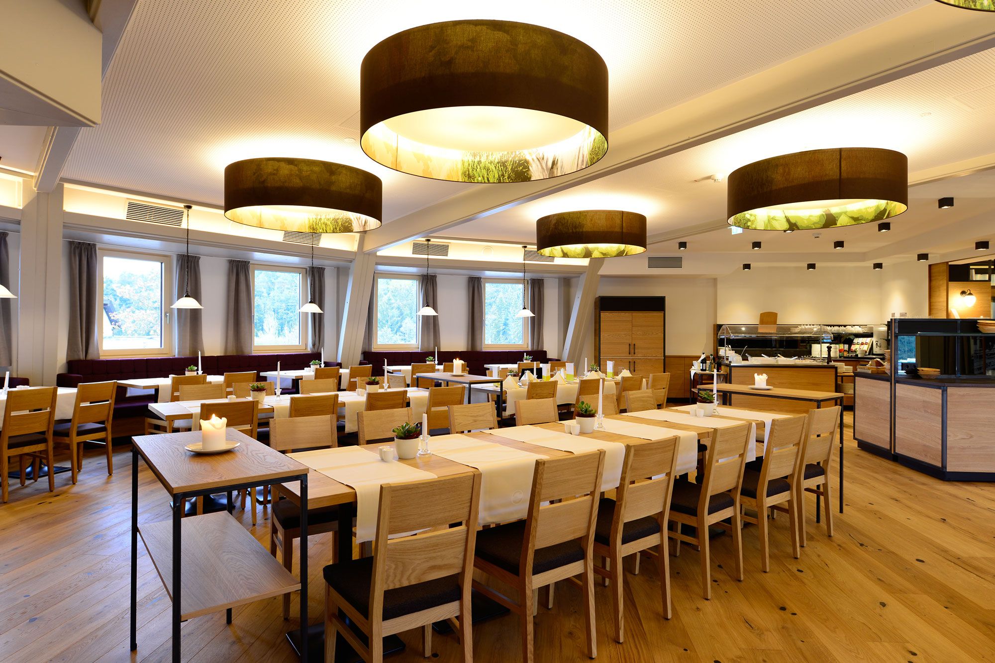 Innenansicht eines modernen Hotelrestaurants mit Holzmöbeln und großen runden Deckenleuchten.