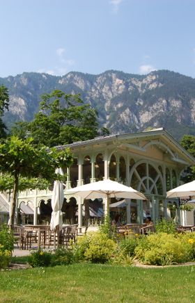 Orangerie Schloss Wartholz, davor eine Terrasse mit Sonnenschirmen und dahinter ein Berg