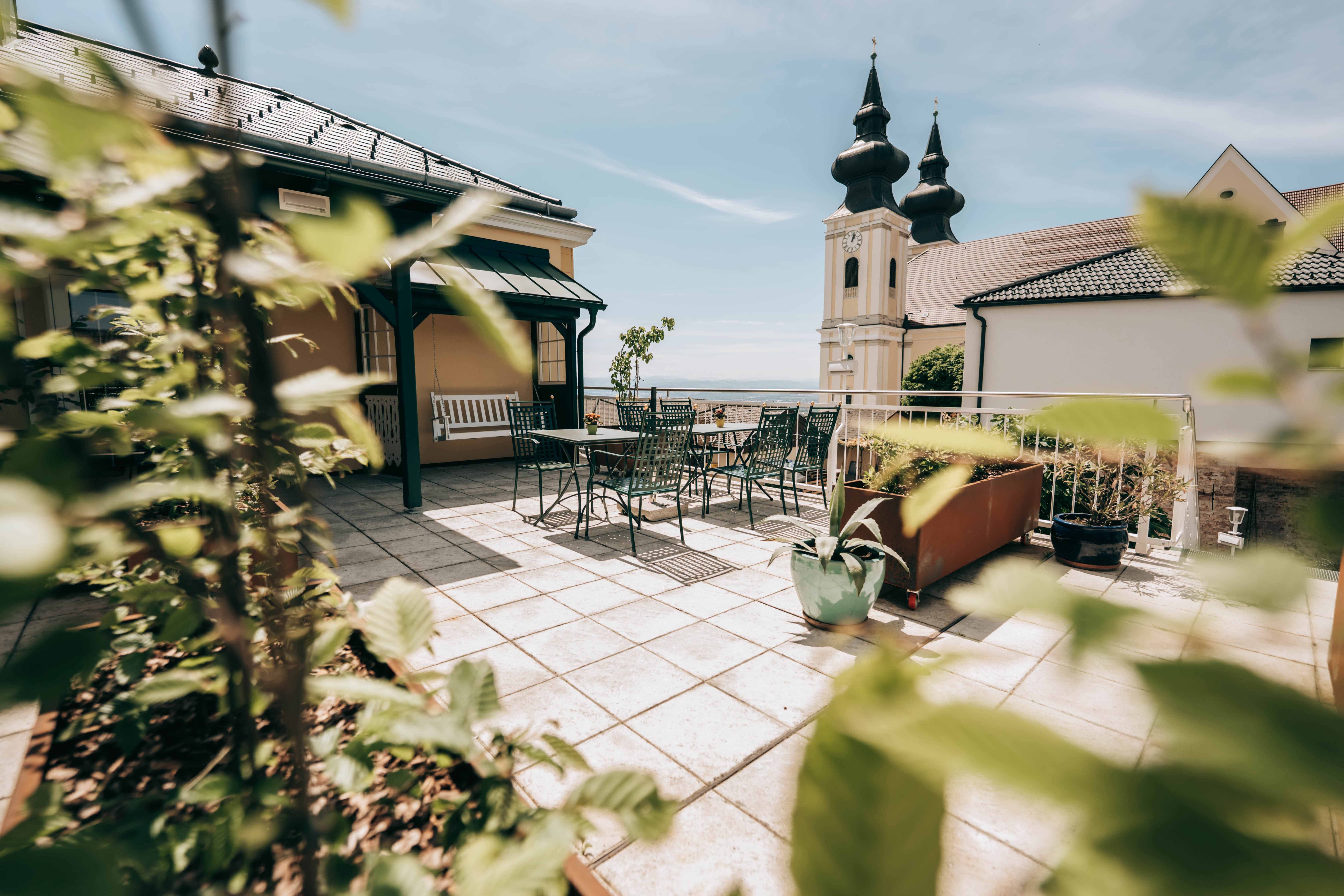 Terrasse mit Tisch und Stühlen, im Hintergrund Kirchturm mit zwei Türmen.
