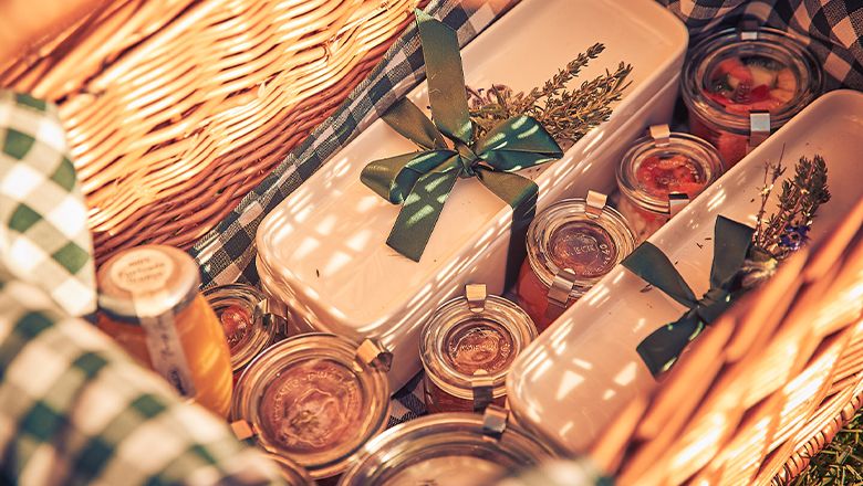 Ein gefüllter Frühstückskorb mit Gläsern und Behältern, dekoriert mit Kräutern und Schleifen.