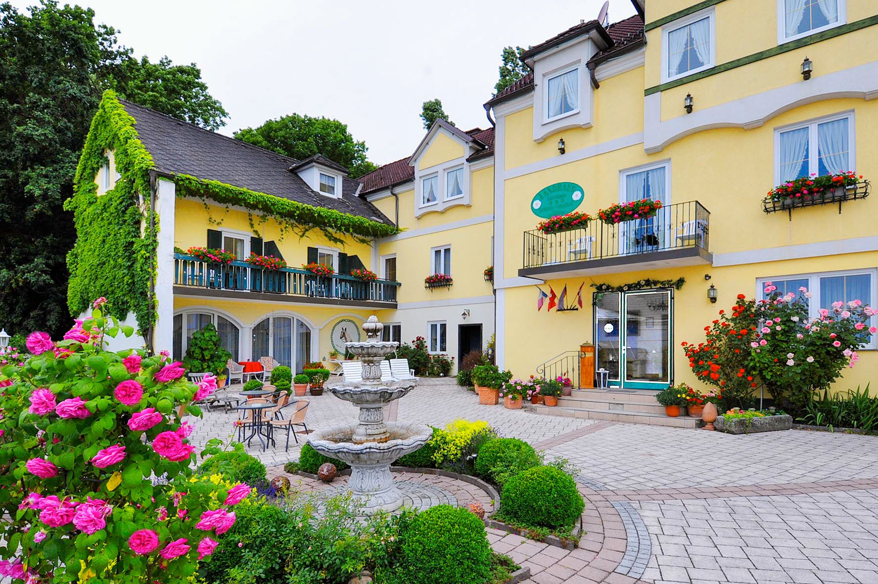 Gelbes Hotelgebäude mit Blumenschmuck und Springbrunnen im Vordergrund.