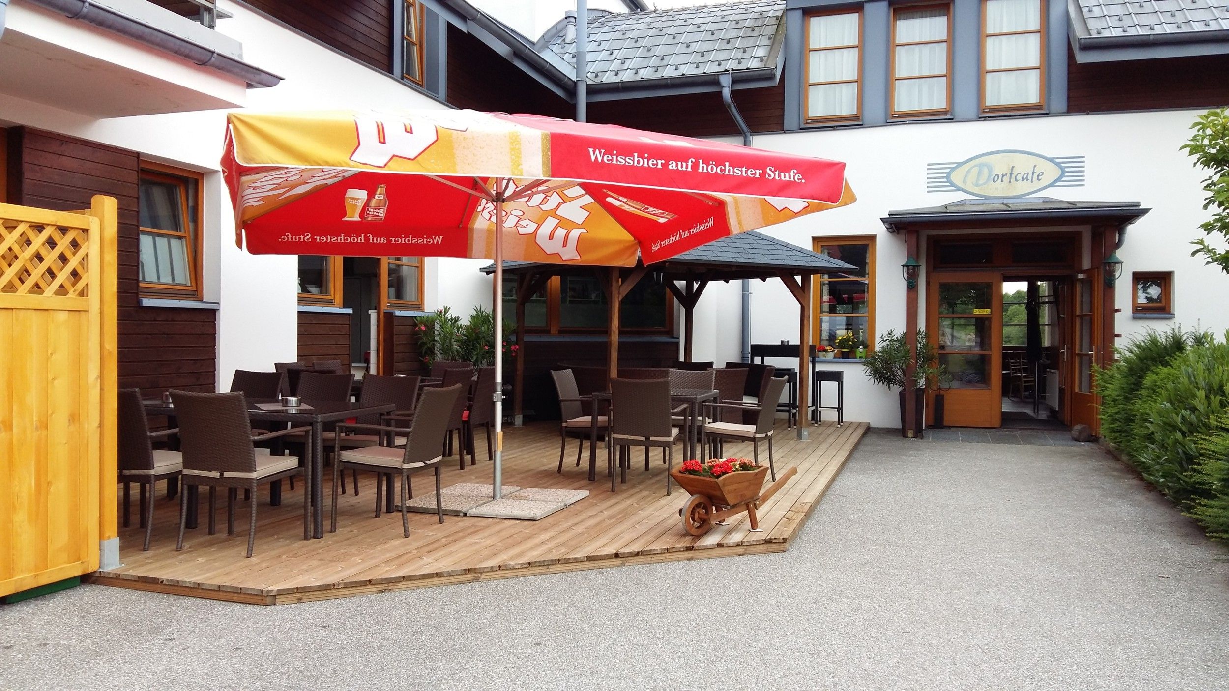 Außenbereich eines Cafés mit Tischen, Stühlen und Sonnenschirmen.