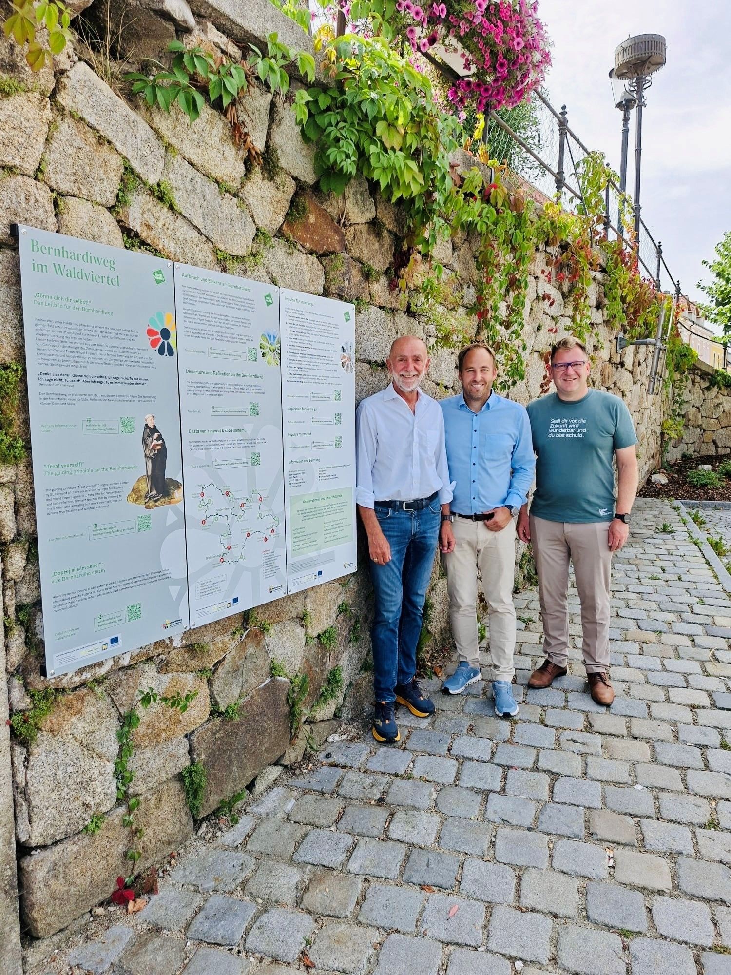 3 Männer neben Tafeln auf einer Steinmauer