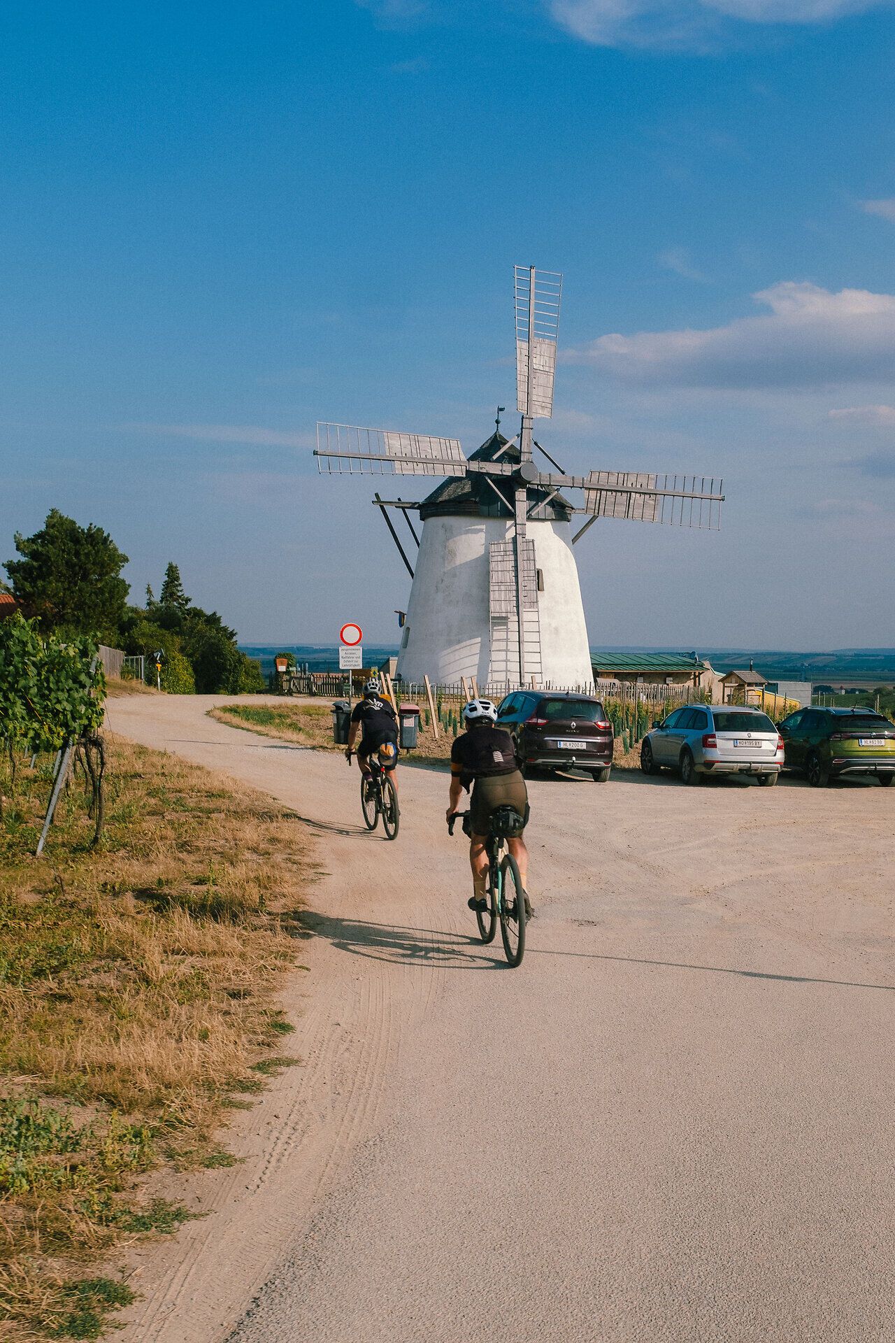 Radfahrer genießen die sanfte Brise und die malerische Landschaft, während sie an einem historischen Windmühlen vorbeifahren. Die idyllische Umgebung lädt dazu ein, die Schönheit der Natur und die Ruhe der ländlichen Gegend zu erleben.