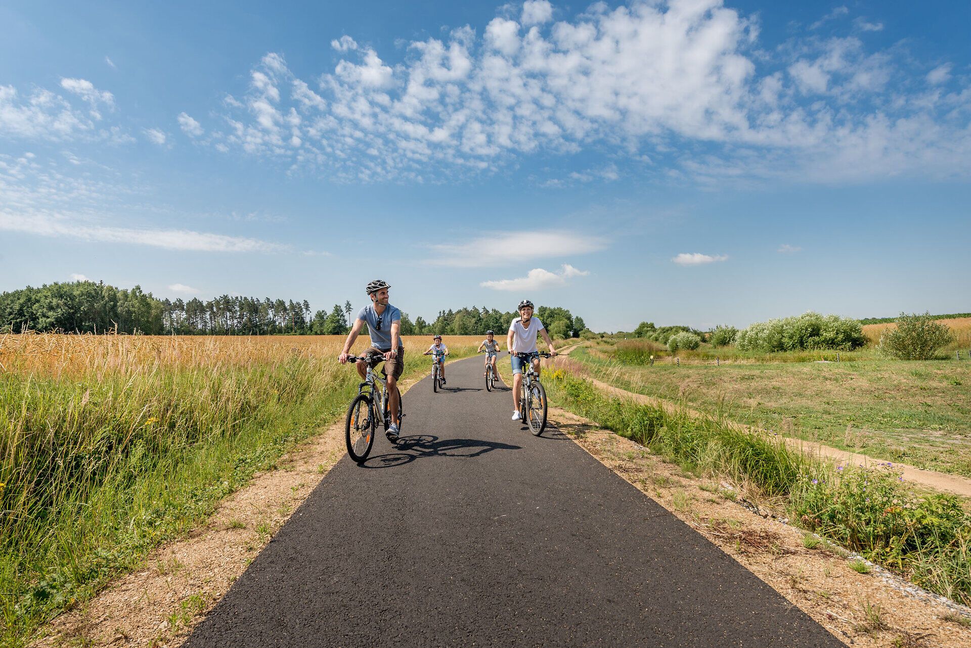 Eine Familie genießt die frische Luft und die malerische Landschaft während einer Radtour. Umgeben von goldenen Feldern und sanften Hügeln strahlt der Sommer eine einladende Wärme aus, die zum Verweilen einlädt.