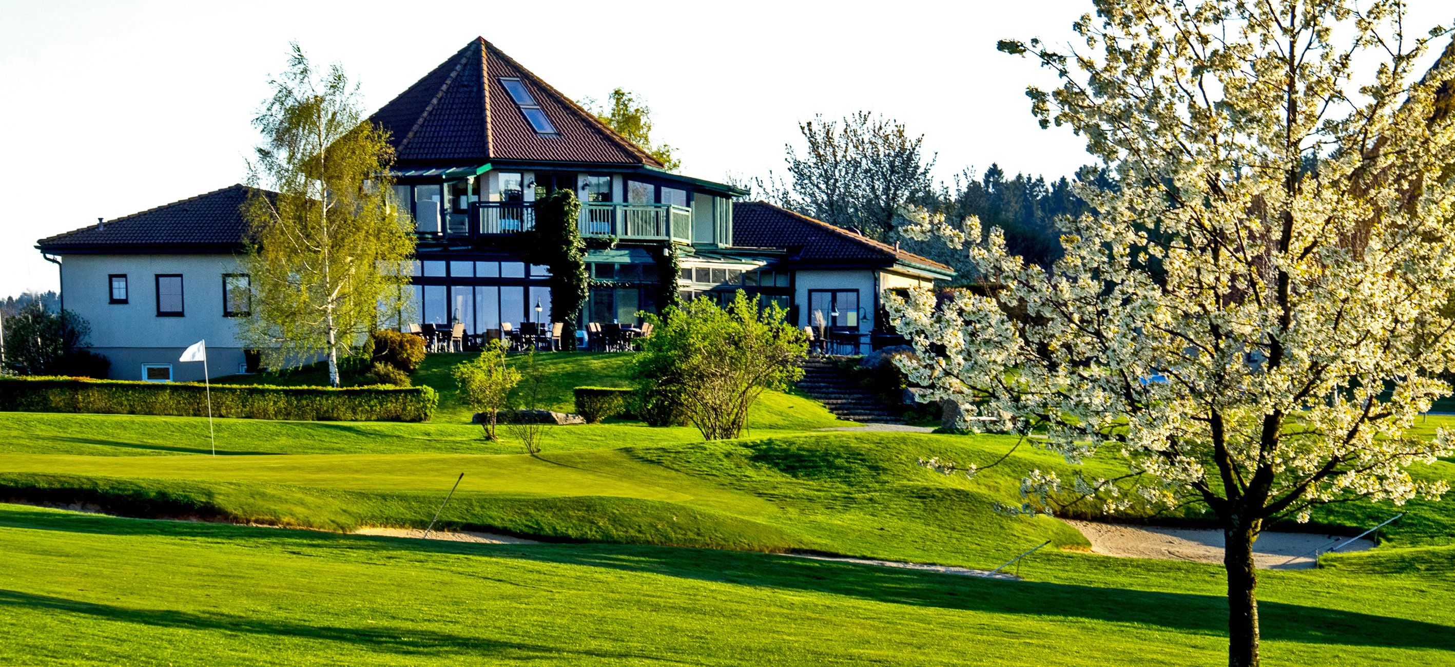 Clubhaus des Golfclubs Ottenstein mit blühendem Baum im Vordergrund.