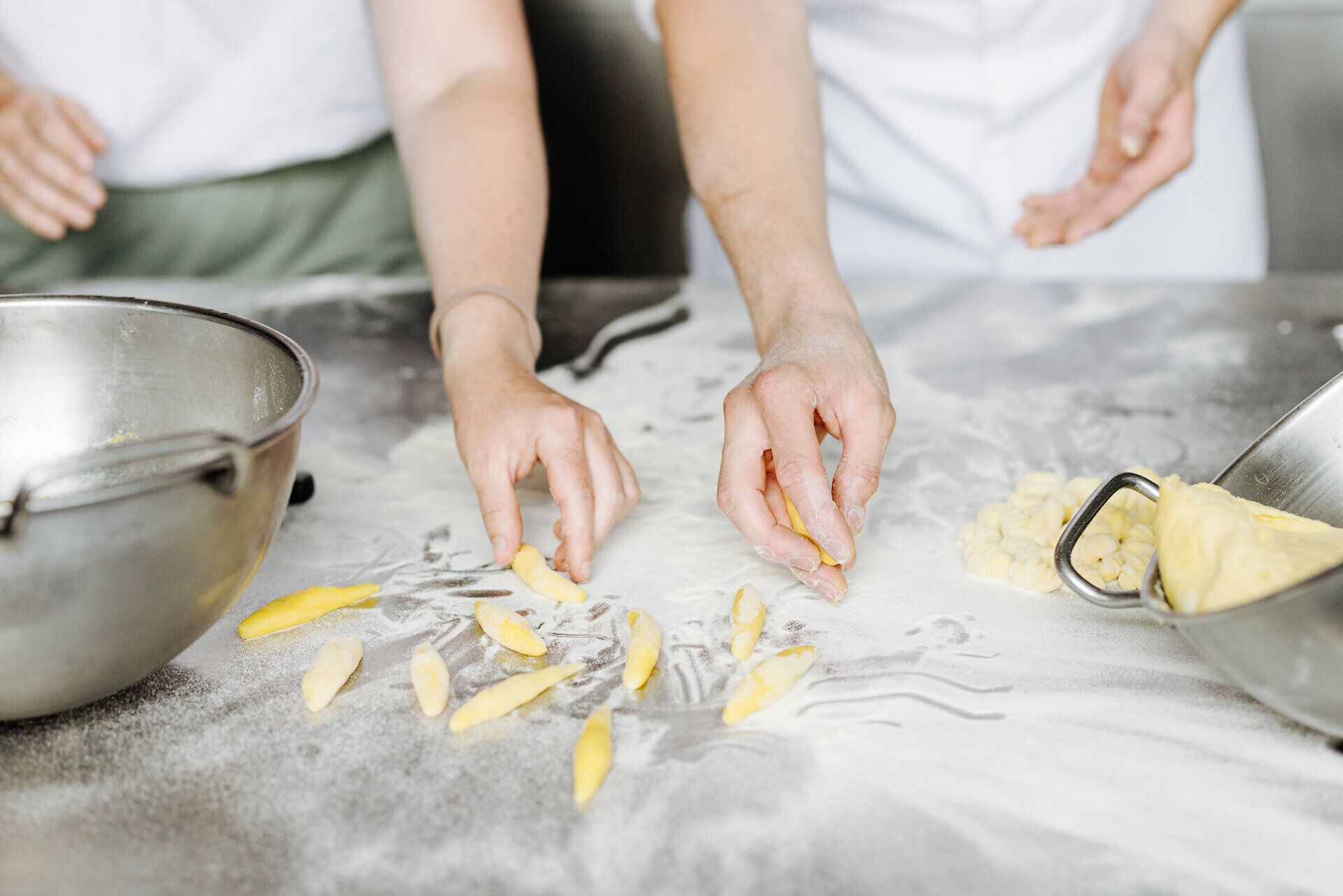 In einer einladenden Küche werden mit Hingabe Mohnnudeln zubereitet. Die Hände der Köche formen liebevoll die Teigstücke, während der feine Mehlstaub in der Luft schwebt und eine gemütliche Atmosphäre schafft.