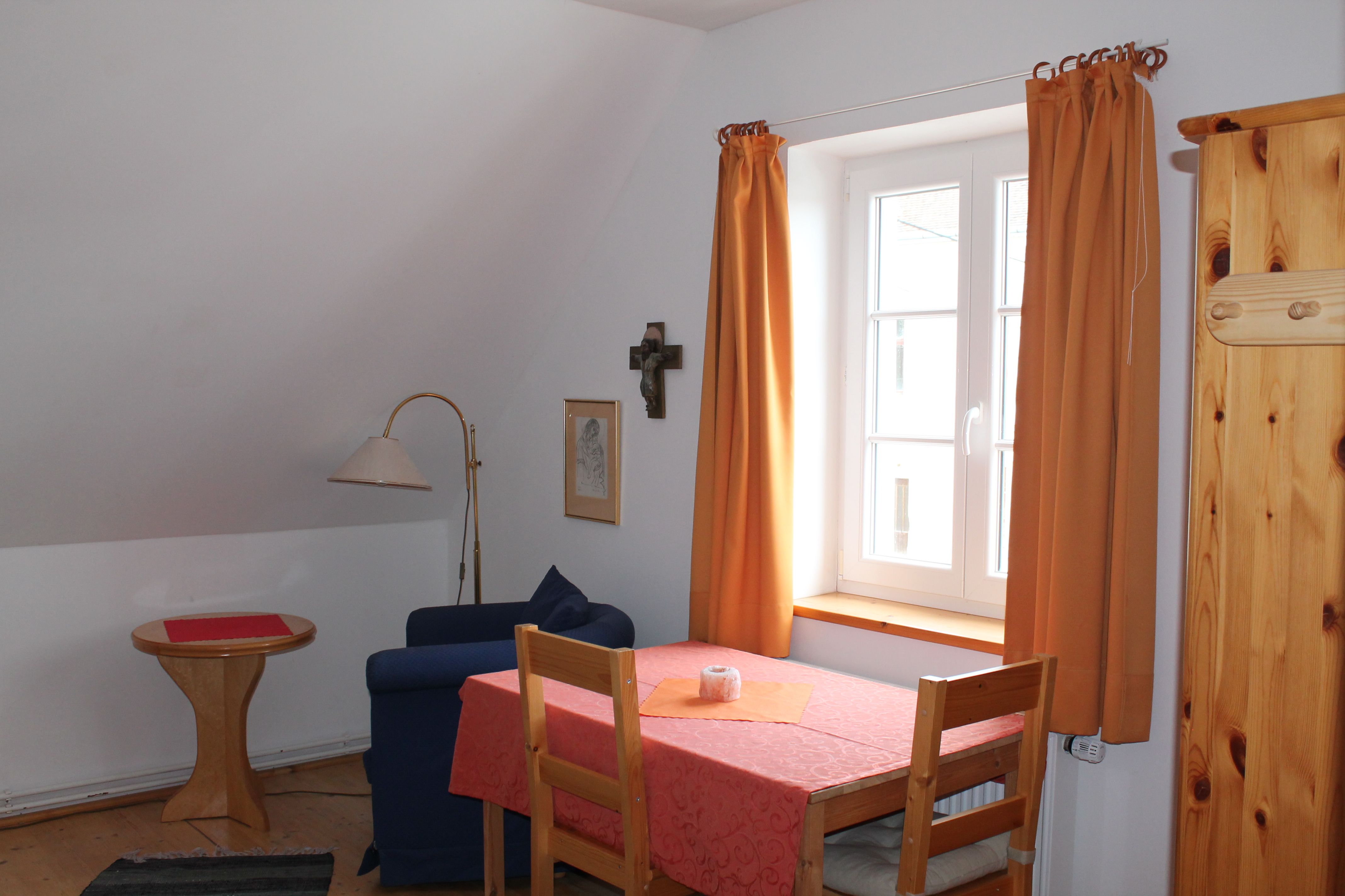 Gemütliches Zimmer mit Tisch, Stühlen, Sofa und Fenster mit orangefarbenen Vorhängen.