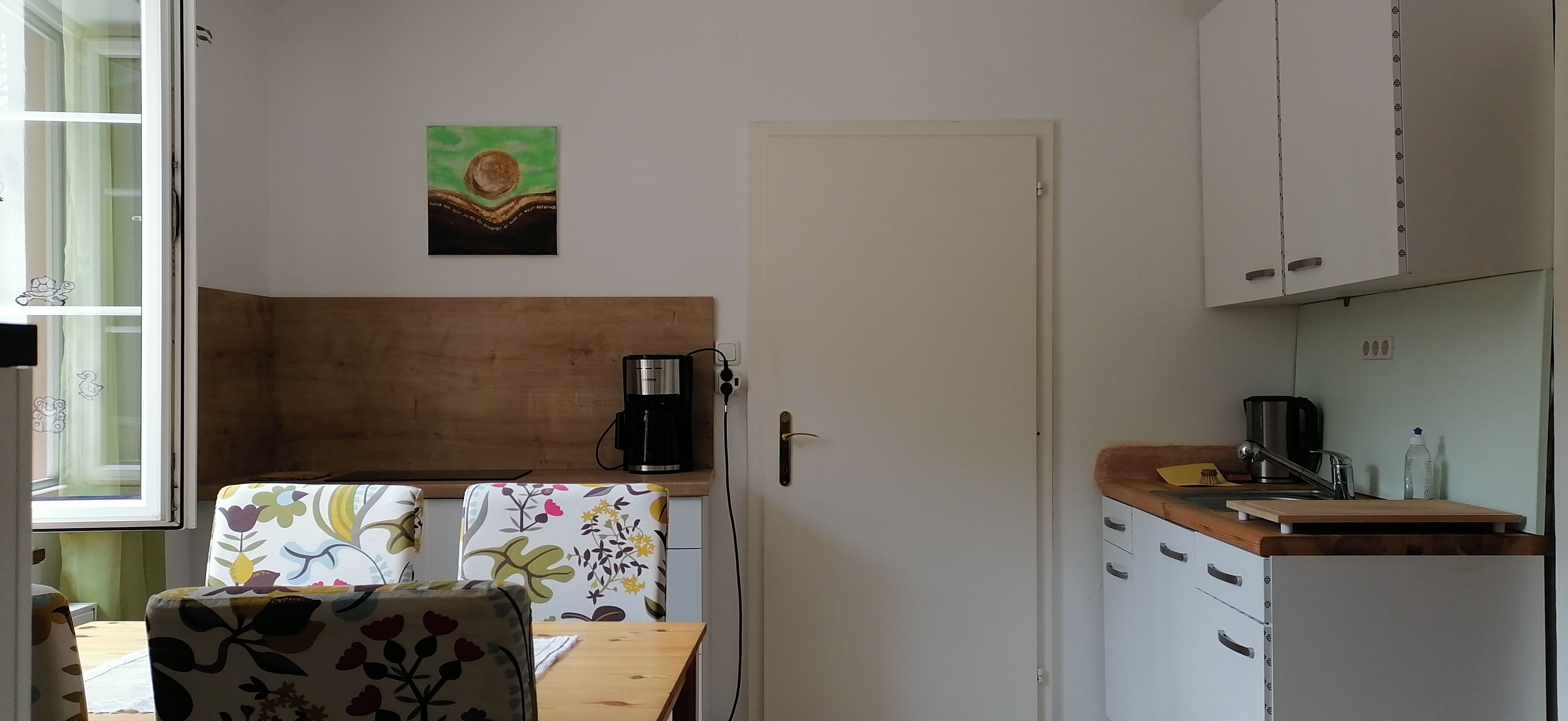 Kleine Küche mit Tisch, Stühlen, Kaffeemaschine und Spüle.