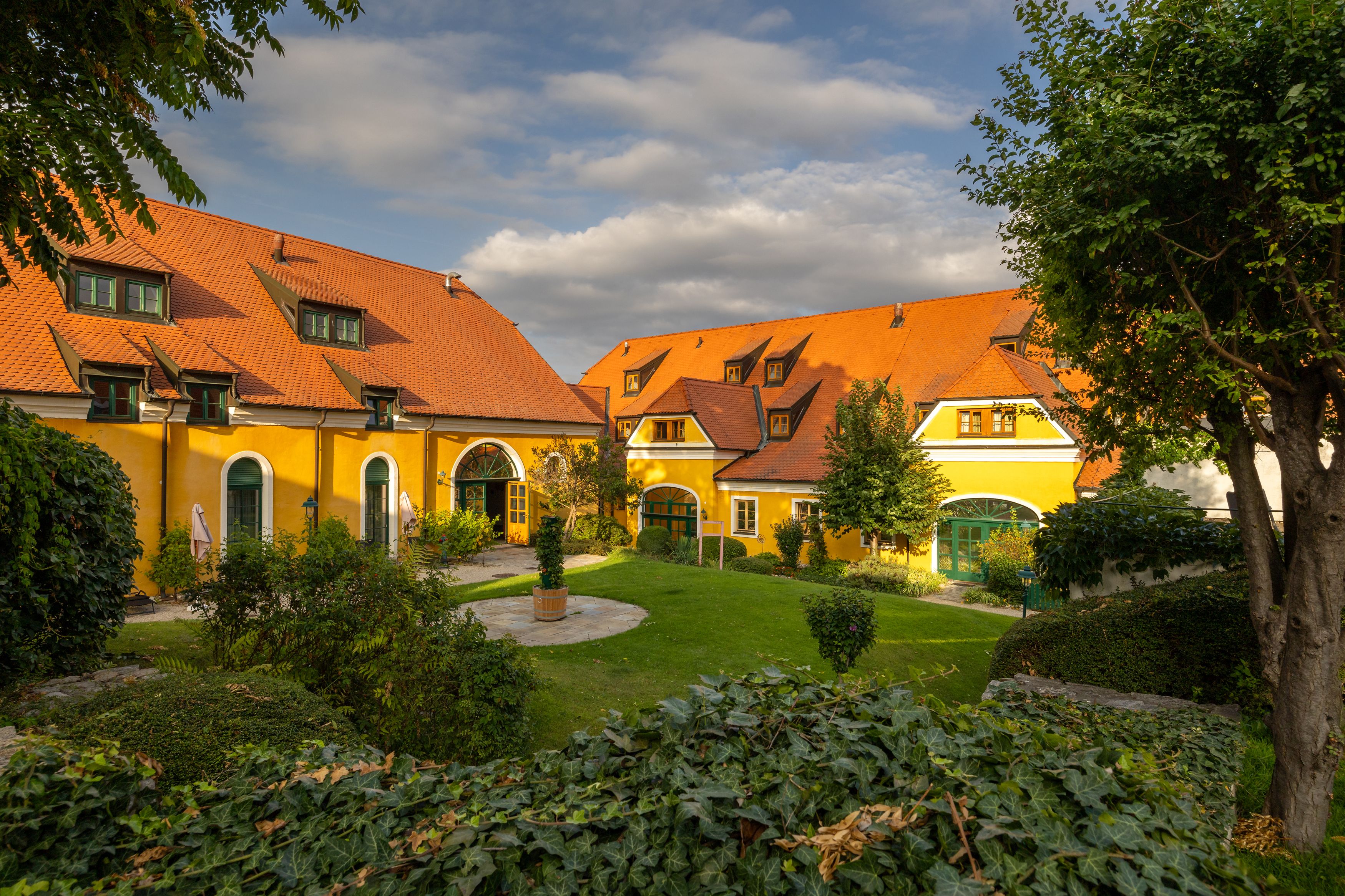 Gelbes Landgut mit roten Dächern und gepflegtem Garten.