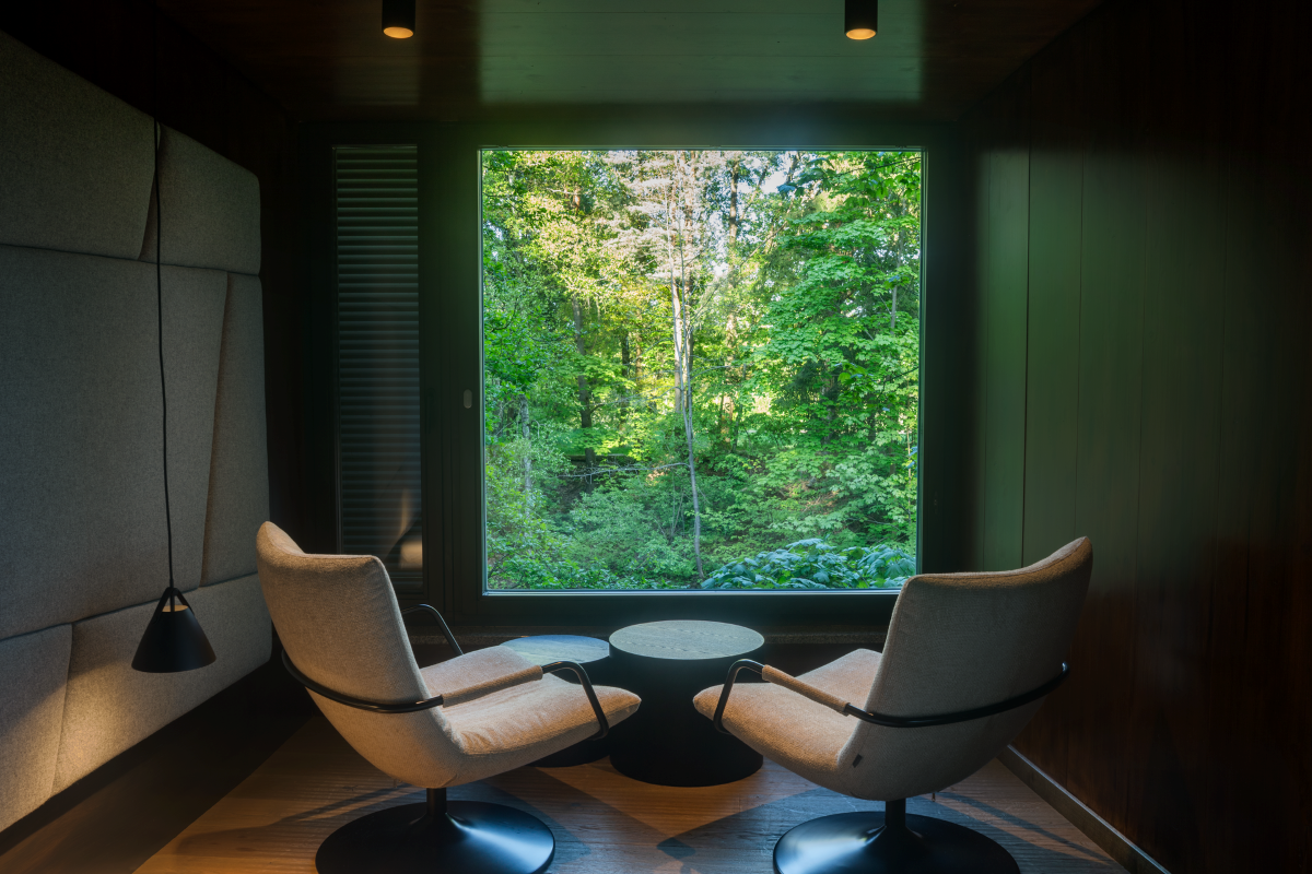 Innenraum eines modernen Baumhauses mit zwei Sesseln und großem Fenster mit Blick auf den Wald.