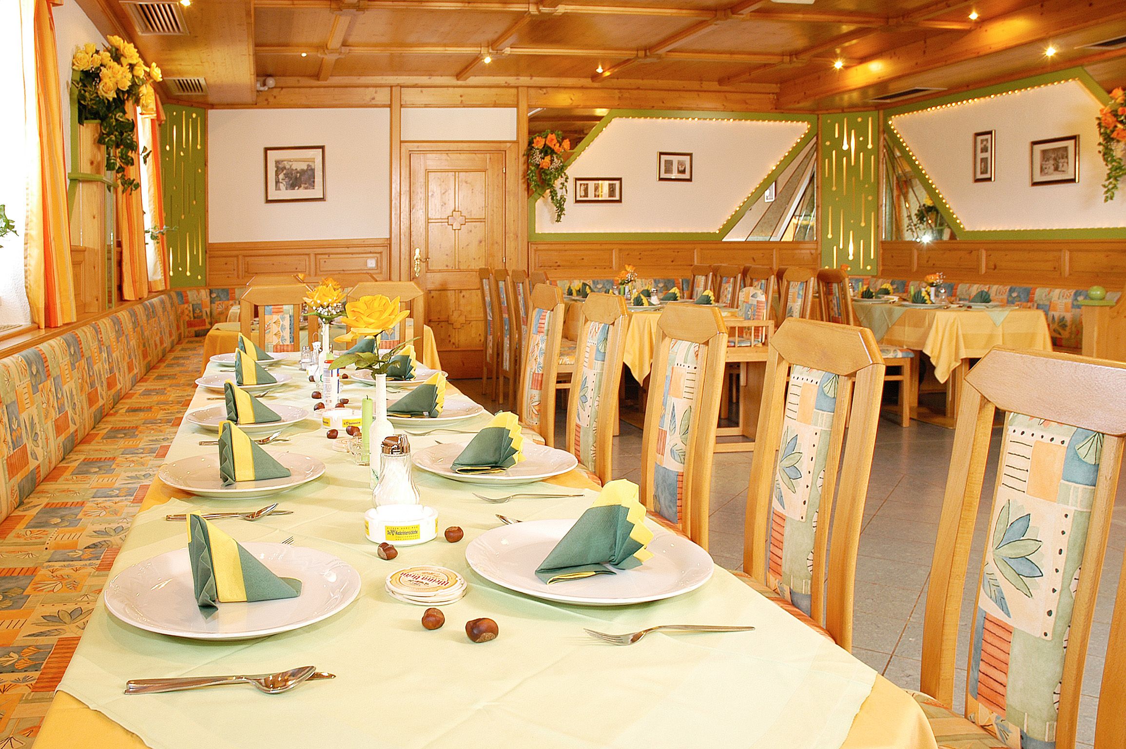 Ein festlich gedeckter Speisesaal mit Holzmöbeln und gelb-grüner Dekoration.