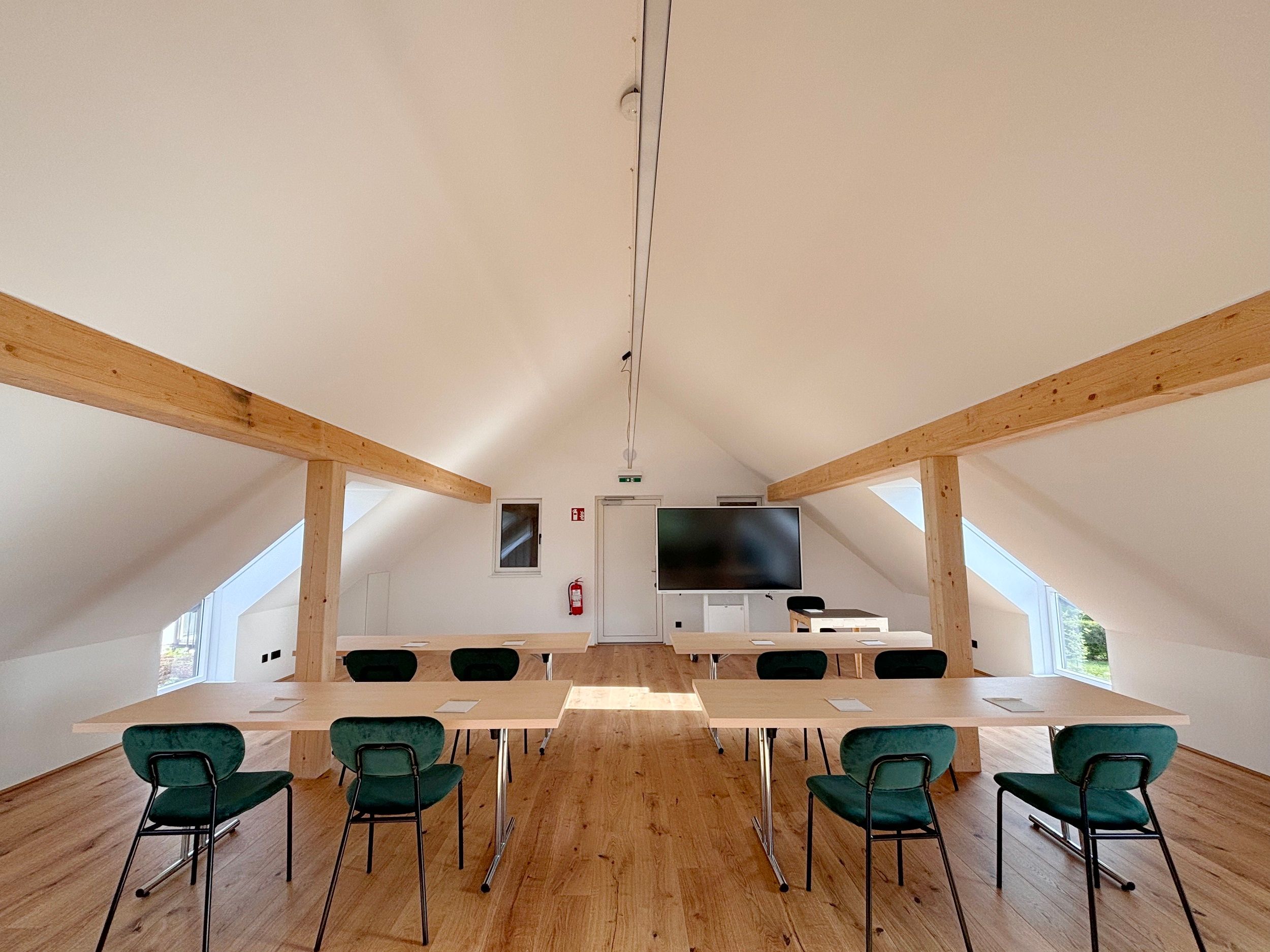 Moderner Seminarraum mit Holzbalken, Tischen und Stühlen.