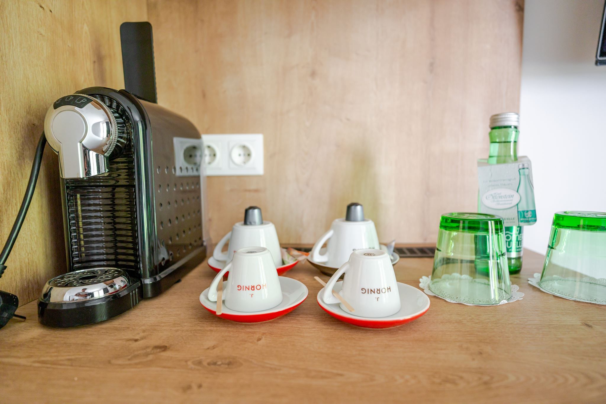 Hotelzimmer-Kaffeestation im Hotel Ottenstein mit Nespresso-Maschine, Tassen, Gläsern und Wasserflasche auf Holzablage.