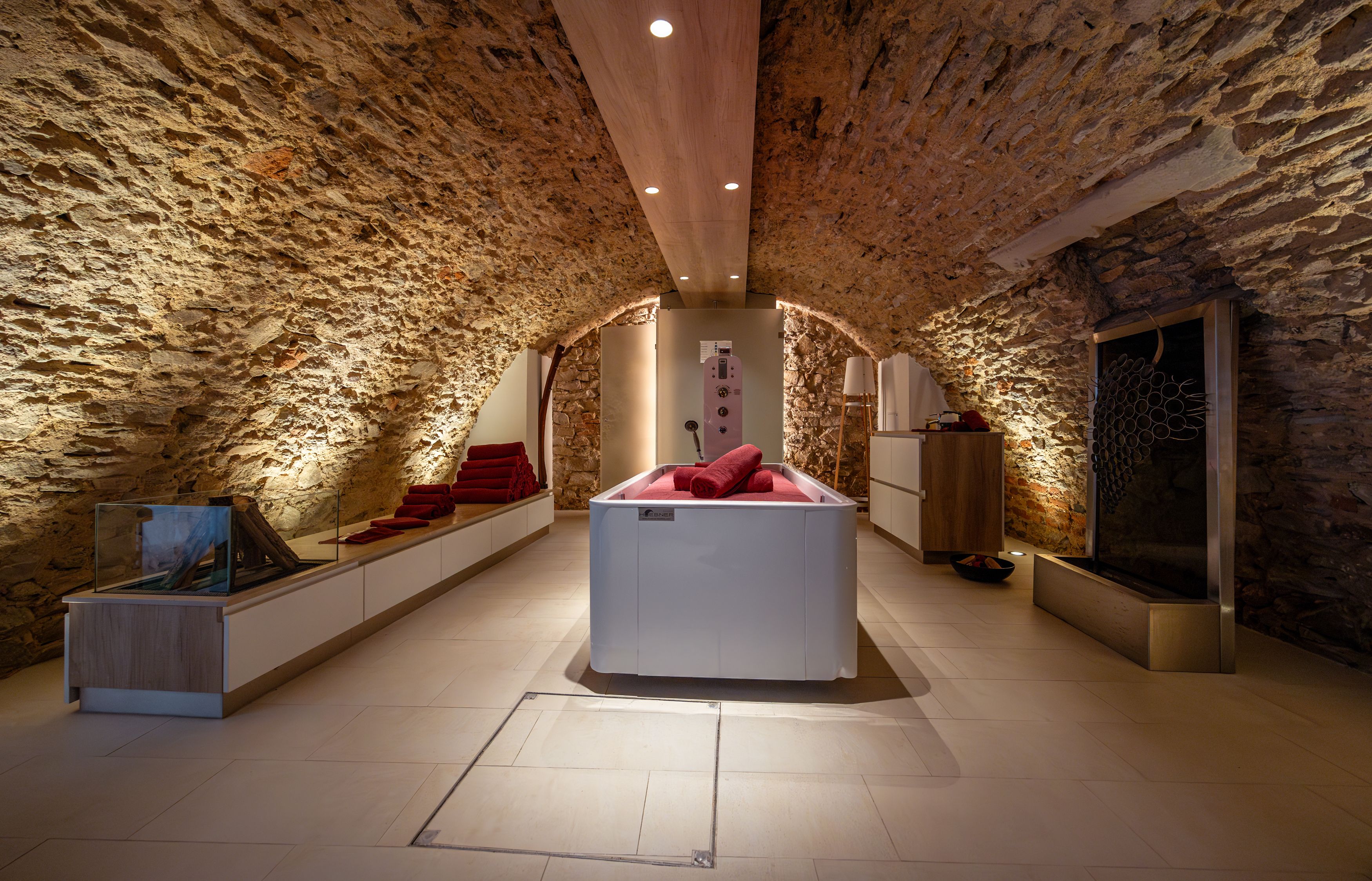 Ein stilvoller Spa-Raum mit Steinwänden, einer modernen Badewanne und roten Handtüchern.