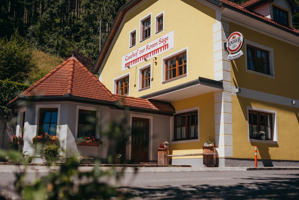 Gelbes Gebäude mit der Aufschrift 'Gasthof zur Roten Säge' und einem Kaiser-Bierschild.