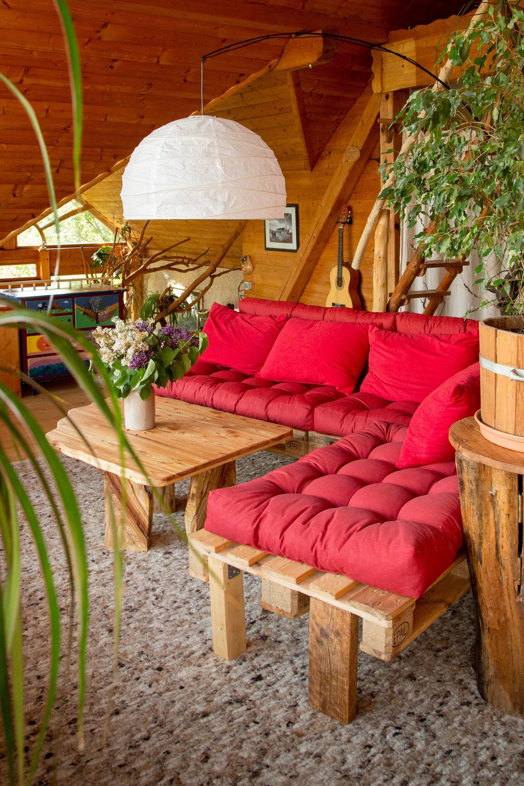 Gemütliches Wohnzimmer mit rotem Sofa, Holzmöbeln, Pflanzen und großer weißer Hängelampe in einer Holzverkleidung.