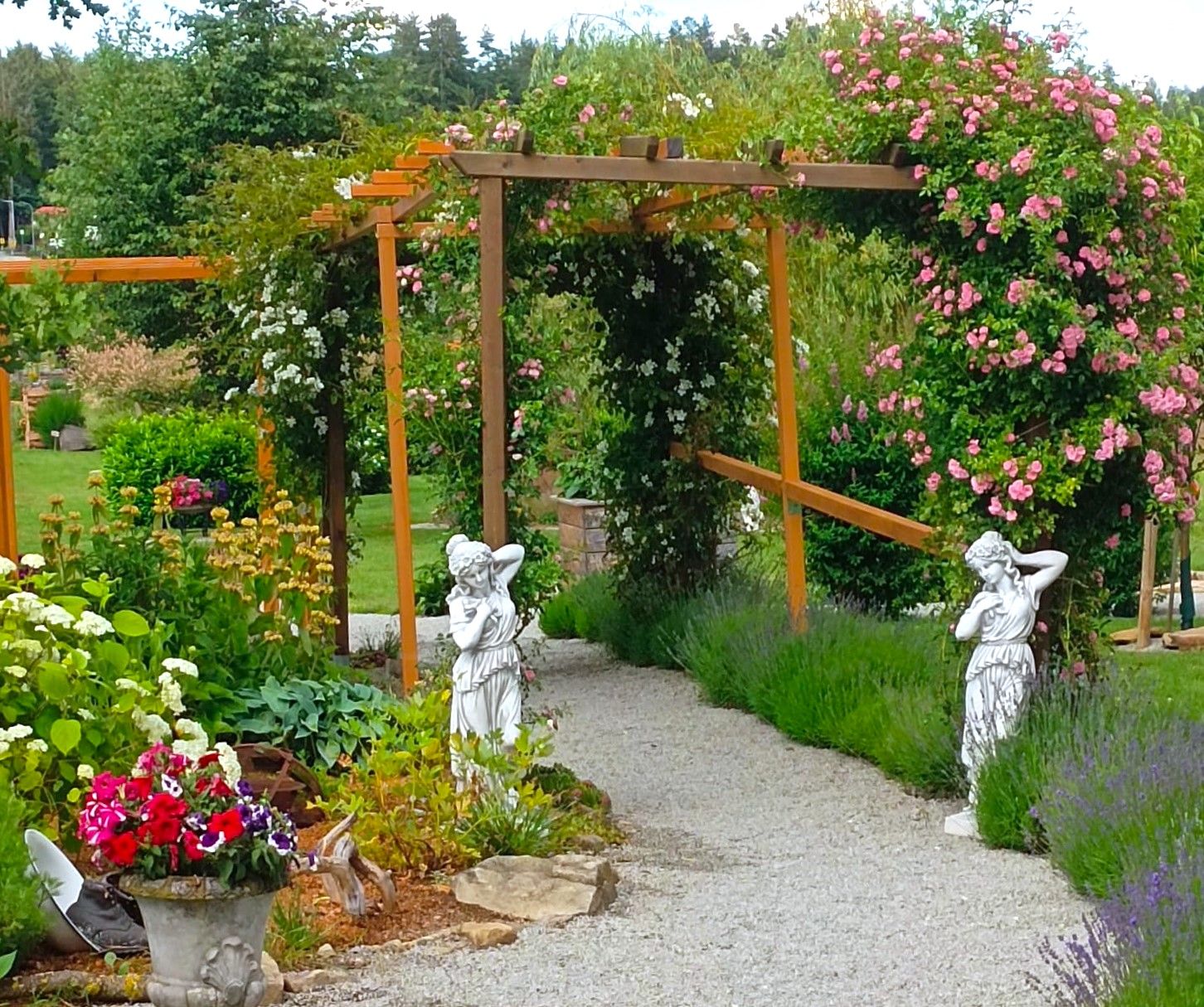 Ein gepflegter Garten mit Rosenbogen, Statuen und blühenden Pflanzen.