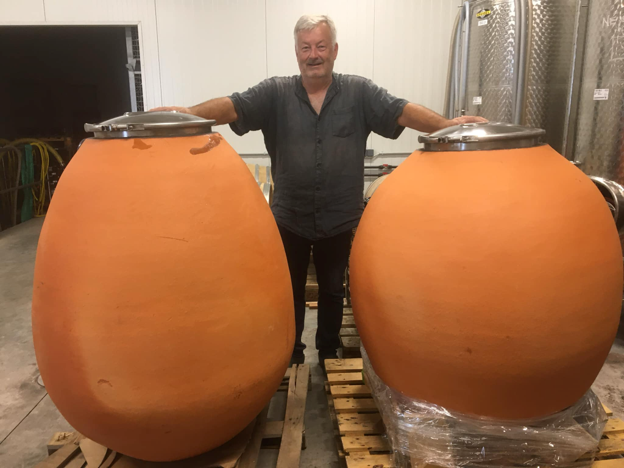 Ein Mann steht zwischen zwei großen, orangefarbenen Tonamphoren in einem Lagerraum.